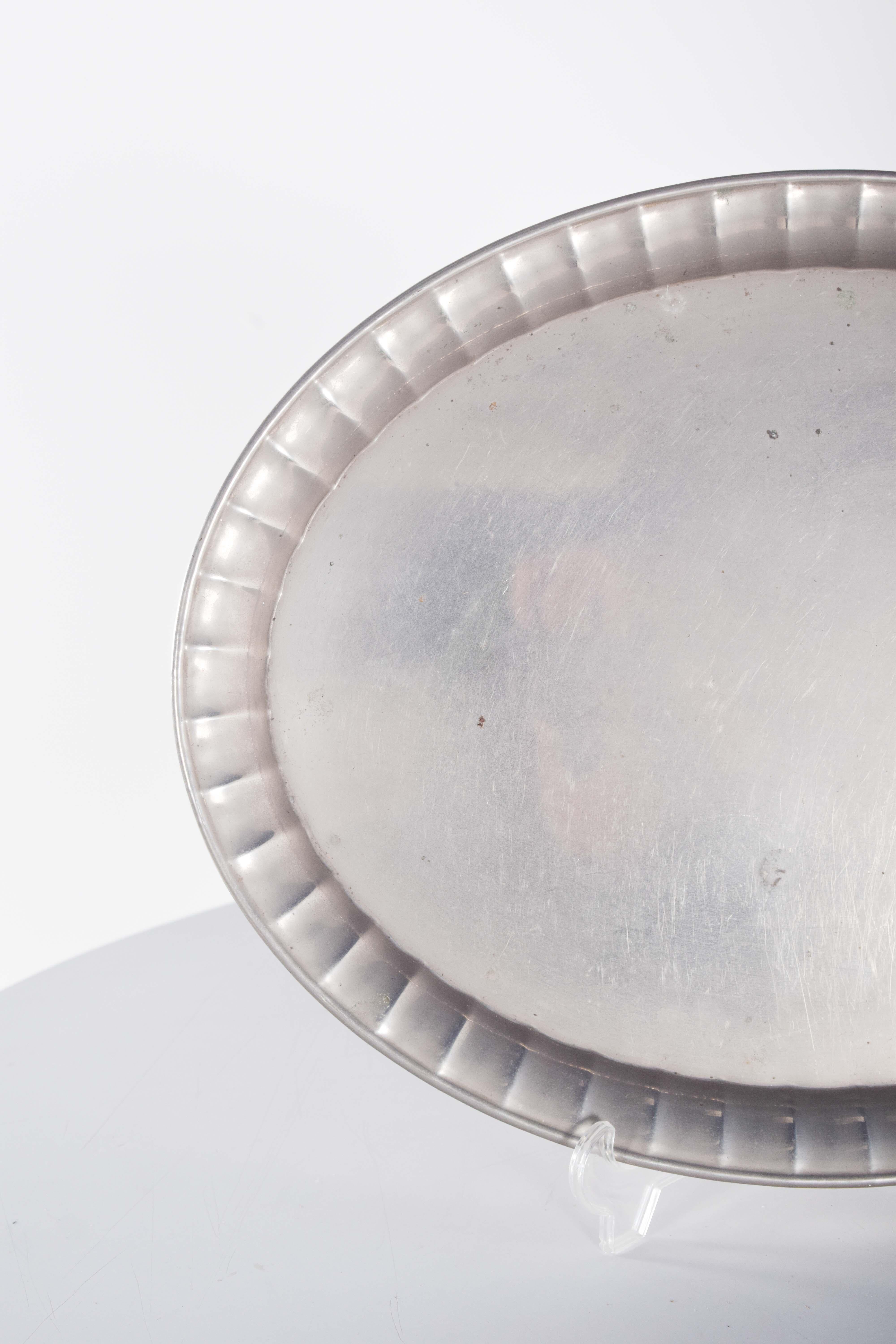 Ovales Metalltablett mit proportionalen Abmessungen, das sowohl zum Servieren als auch als dekoratives Element verwendet werden kann.
Der Rand ist geprägt und durchbrochen, mit geraden und gleichmäßigen Rillen. Die Oberfläche ist glatt und poliert,
