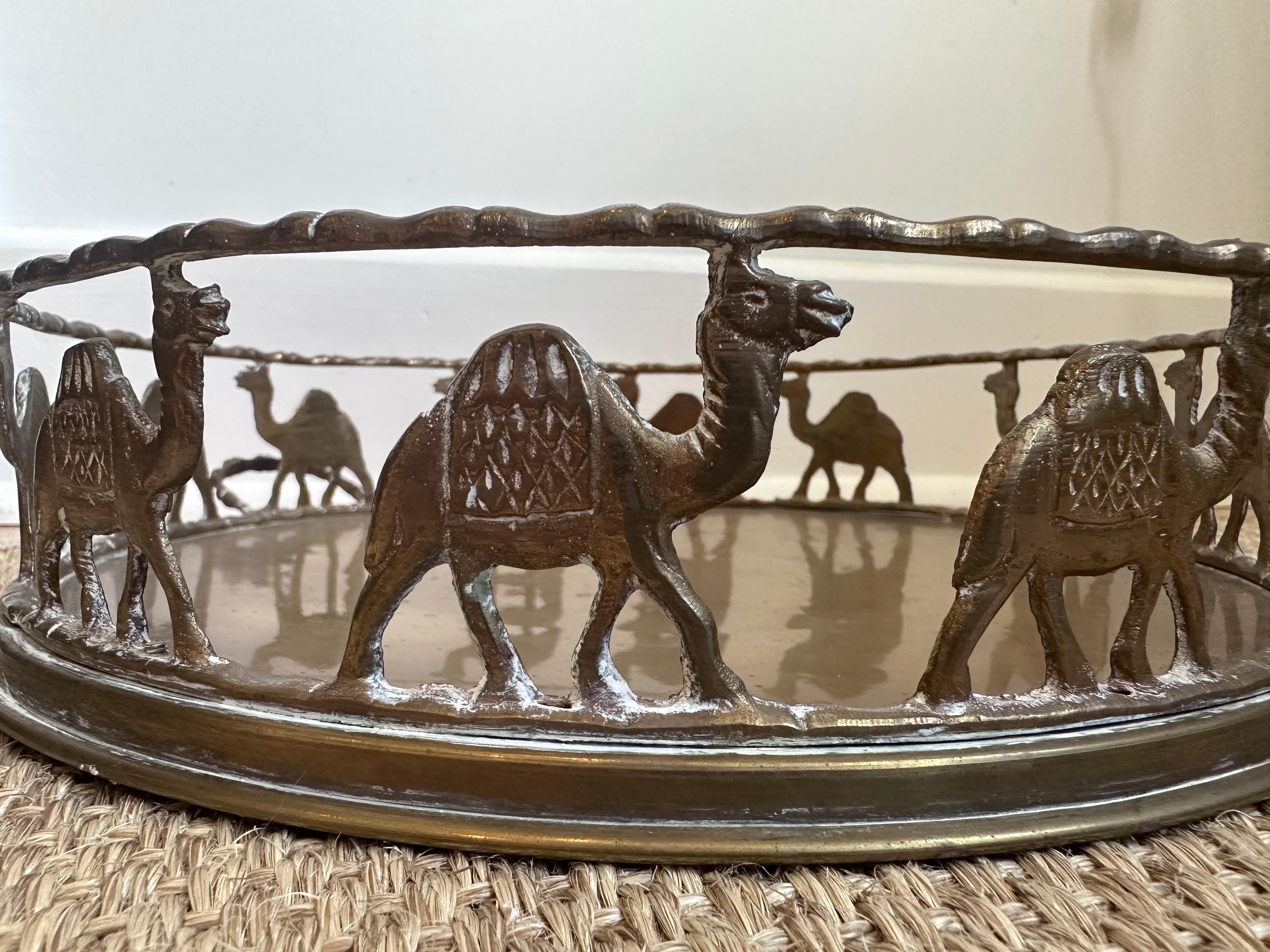 This is a decorative round brass tray with an ornate design featuring a procession of camels. The tray has a metal base, encircled by a raised brass-like gallery formed by repeated cutout figures of camels, each with distinctive detailing such as