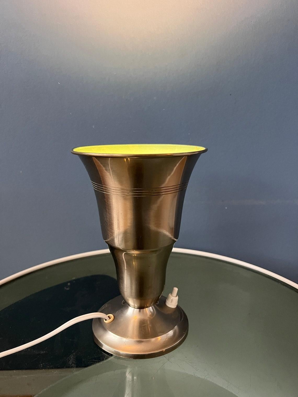Lampe de table Uplighter 'Cup' en métal en forme de trompette. La lumière est bien projetée vers le haut et se reflète bien sur la surface argentée. La lampe peut être allumée et éteinte à l'aide d'un bouton situé sur la base. La lampe nécessite une