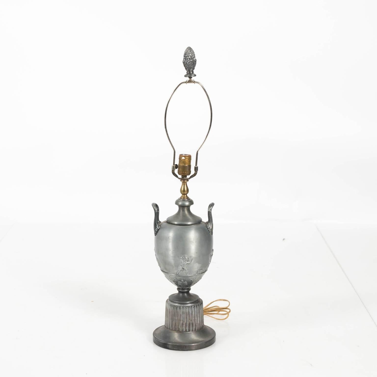 Contemporary metal urn lamp that features repoussé Putti on the body with matching pleated shade, circa late 20th century.
 