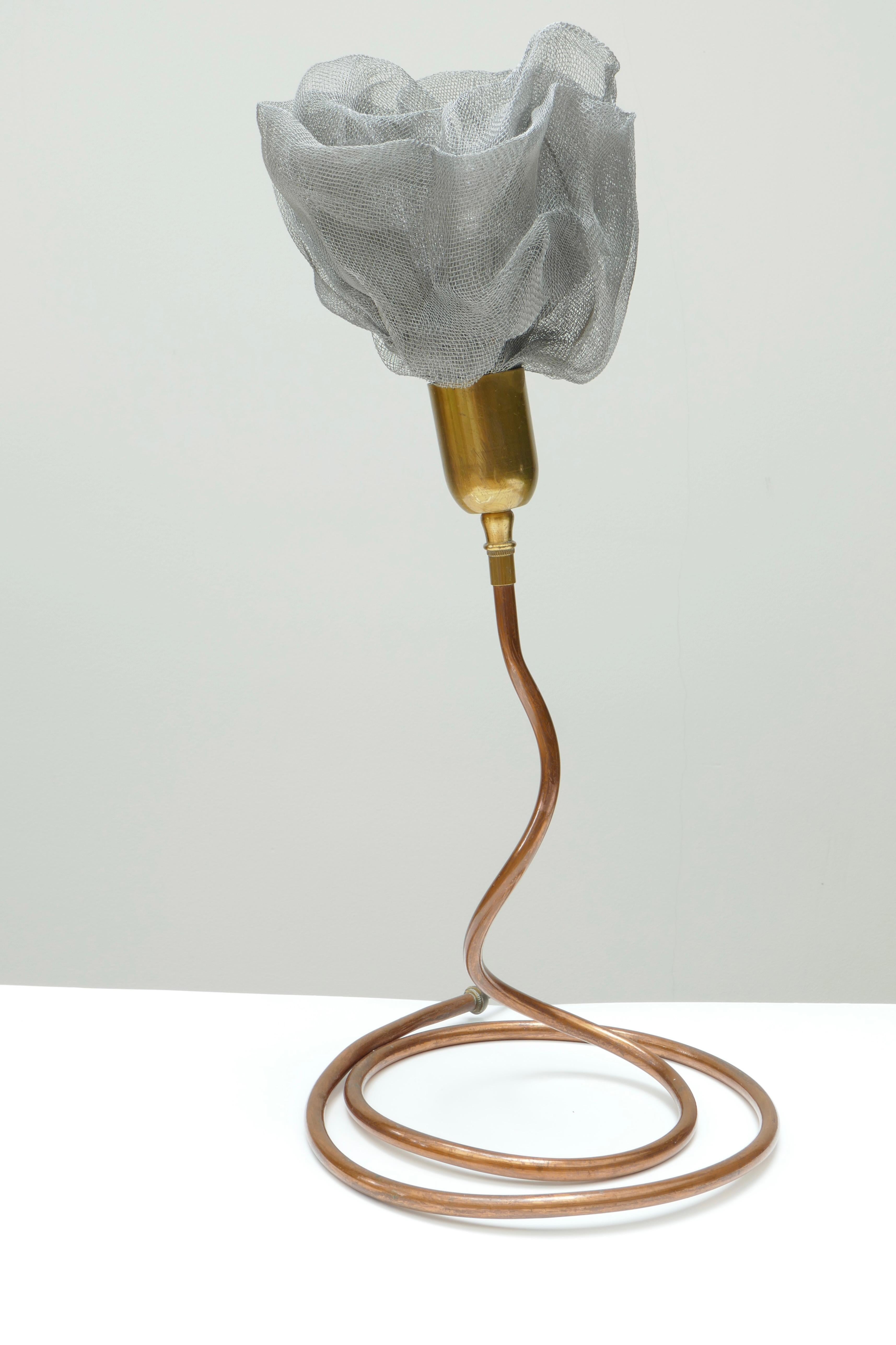 A unique and original table lamp with a serpent or flexible copper base and stem and a lamp holder shaped as a flower. The flower is made of woven mesh metal or tulle. The sepal of the flower is in brass.
The copper base has a diameter of 24 cm