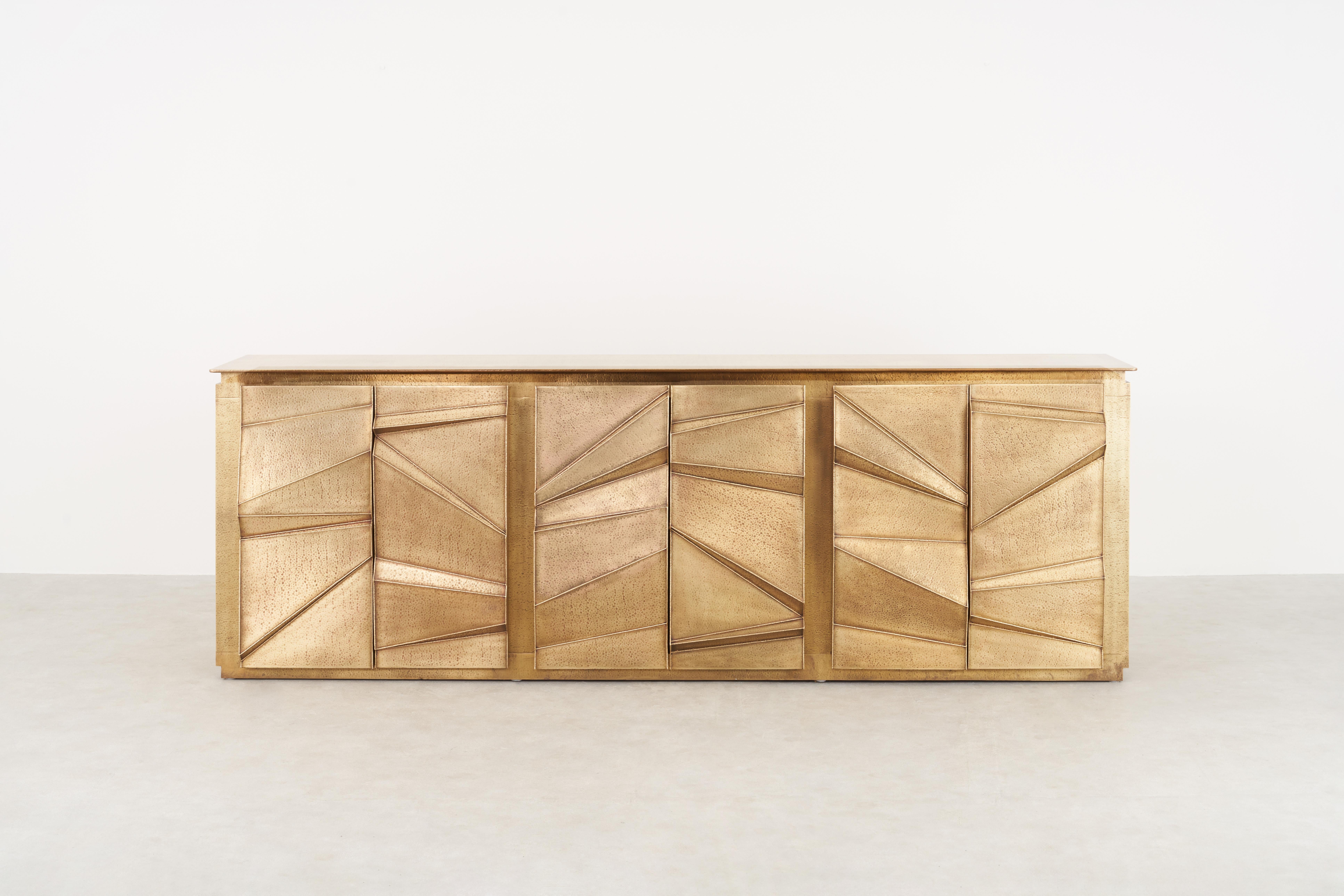 The facade of this sculptural cabinet is crafted using the studio’s signature Hollowed Joinery technique–merging materials and processes that feature hammered brass sheet metal, welded together to leave a hollow structure within. The patinated gold