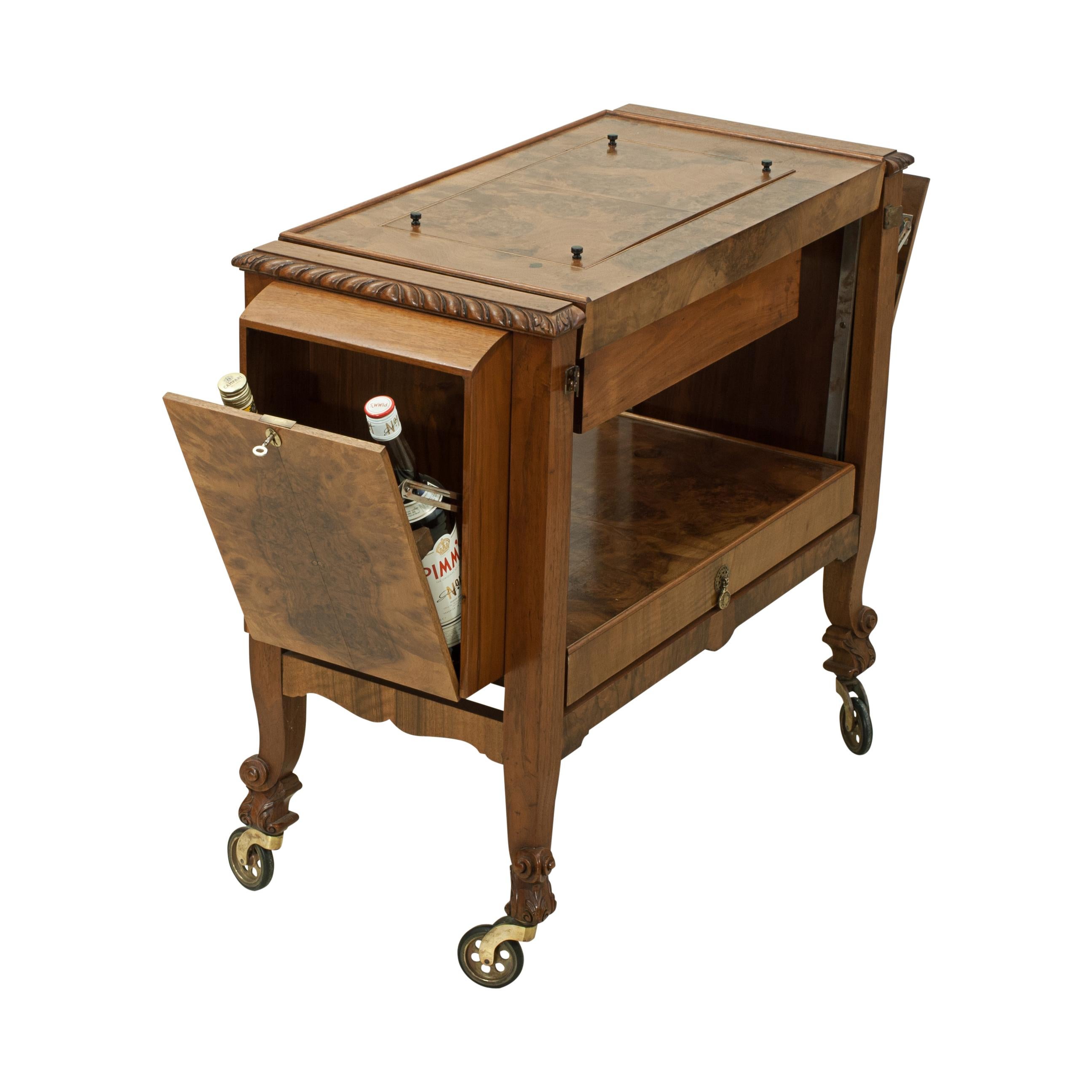 A mid-20th century walnut veneered metamorphic cocktail trolley. The top has a lift-off section that's doubles as a serving tray and when removed reveals a central fitted well which includes a plated cocktail Shaker and two glass bottles (there are