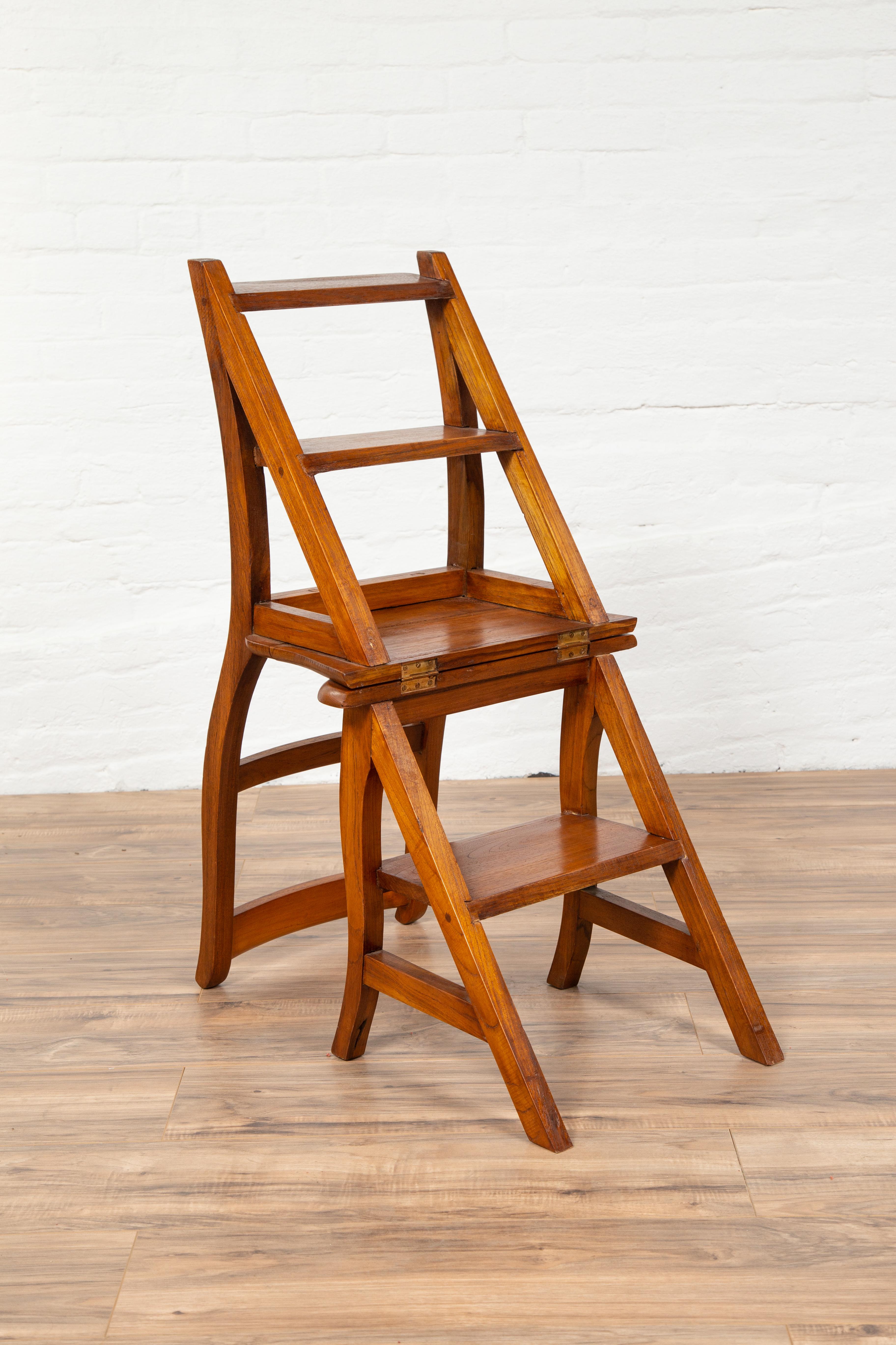 A vintage Indonesian teak wood Dutch Colonial metamorphic ladder chair from the midcentury period. This exquisite and convenient teak wood step ladder features a linear silhouette, accented by the delicate curvy presence of its rear legs. Unfolding