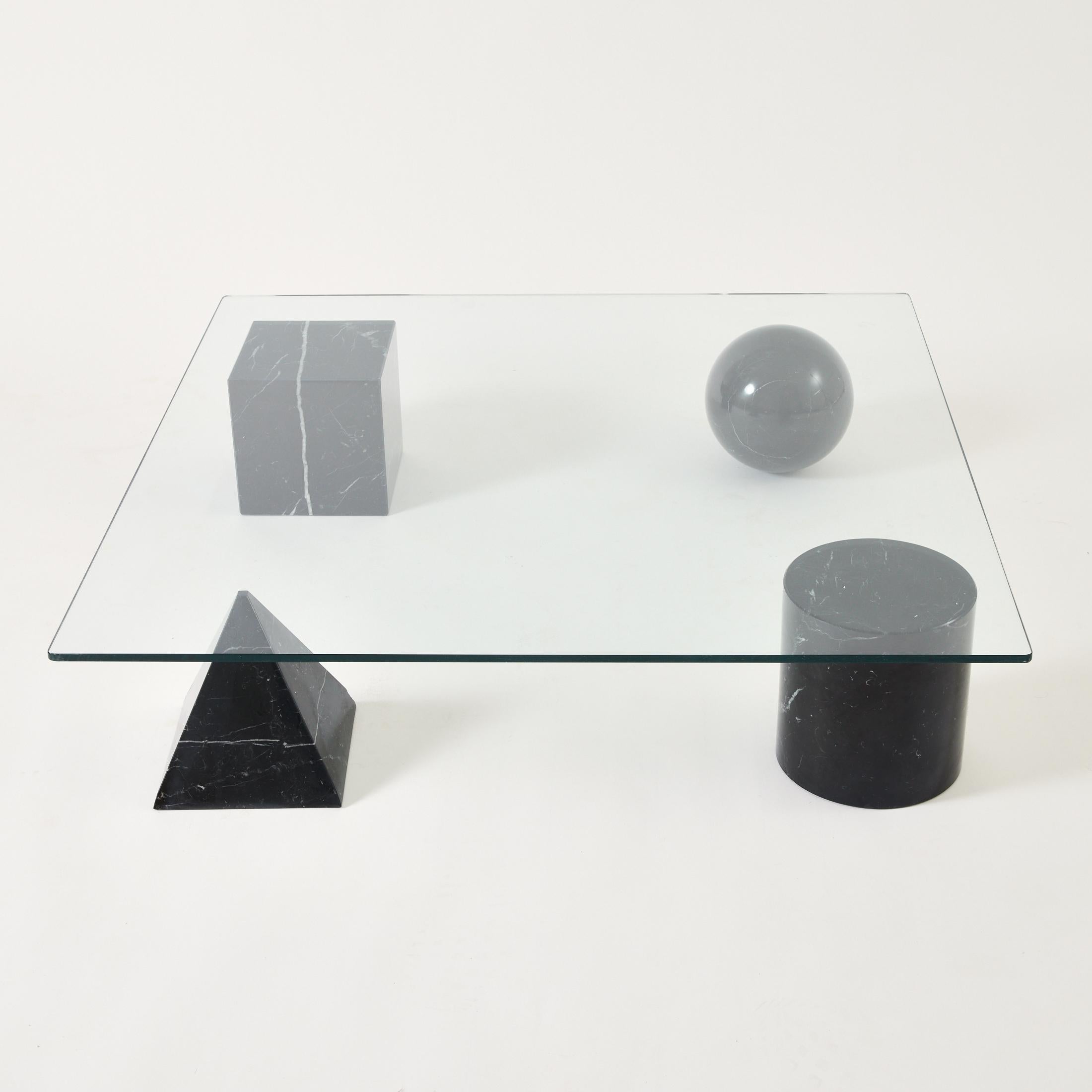 Metaphora table designed by Massimo and Lella Vignelli in 1979 for Martinelli Luce. A glass top sits upon four black marquina marble shapes which represent the four forms of Euclidean geometry. The sphere represents the globe, the pyramid represents