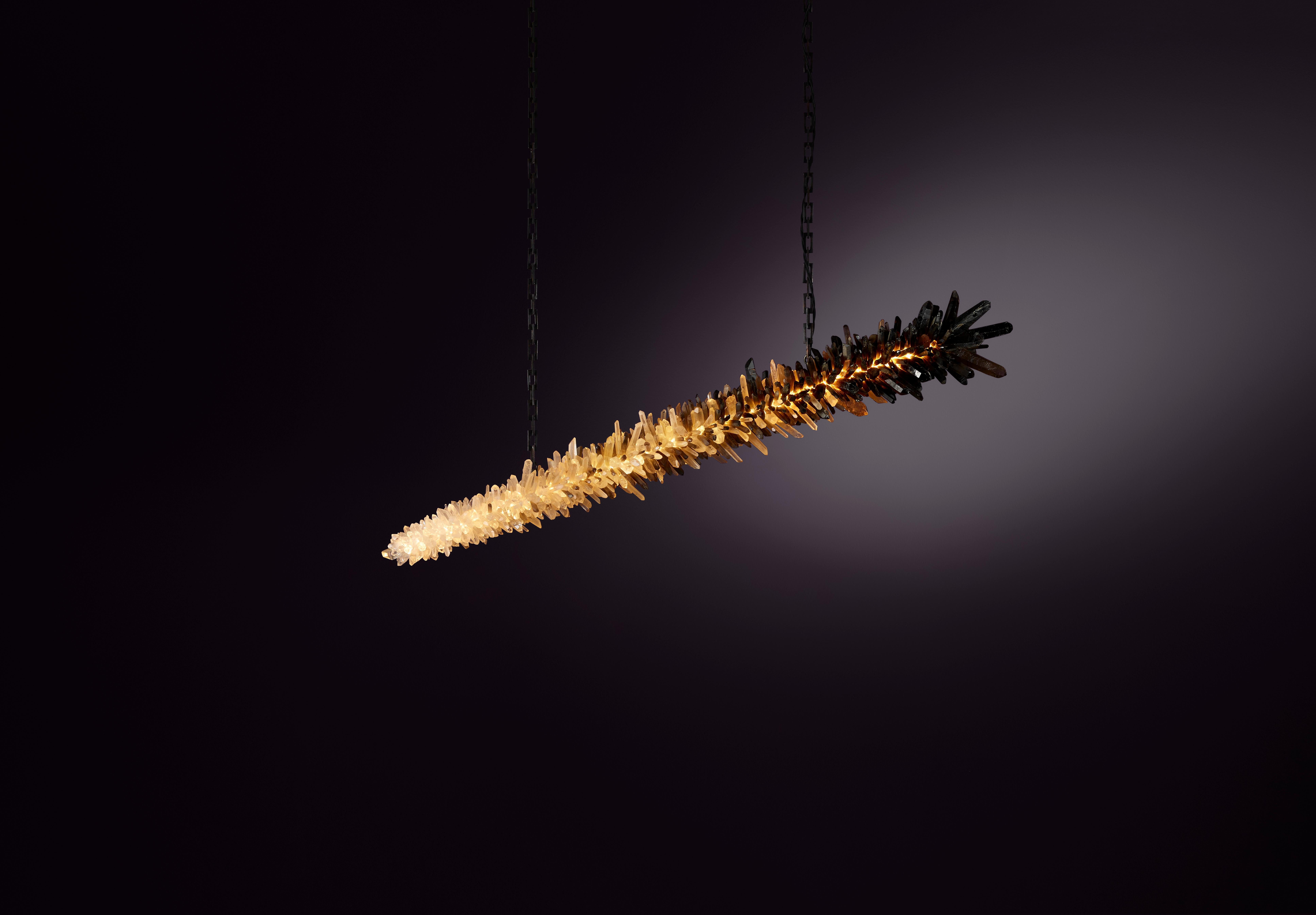Lampada a sospensione Meteor 120 di Christopher Boots
Dimensioni: D 25 x L 120 x H 25 cm.
Materiali: Cristalli di quarzo chiaro naturalmente non tagliati, cristalli di quarzo fumé naturalmente non tagliati, ottone invecchiato.

Disponibile in 90 cm,