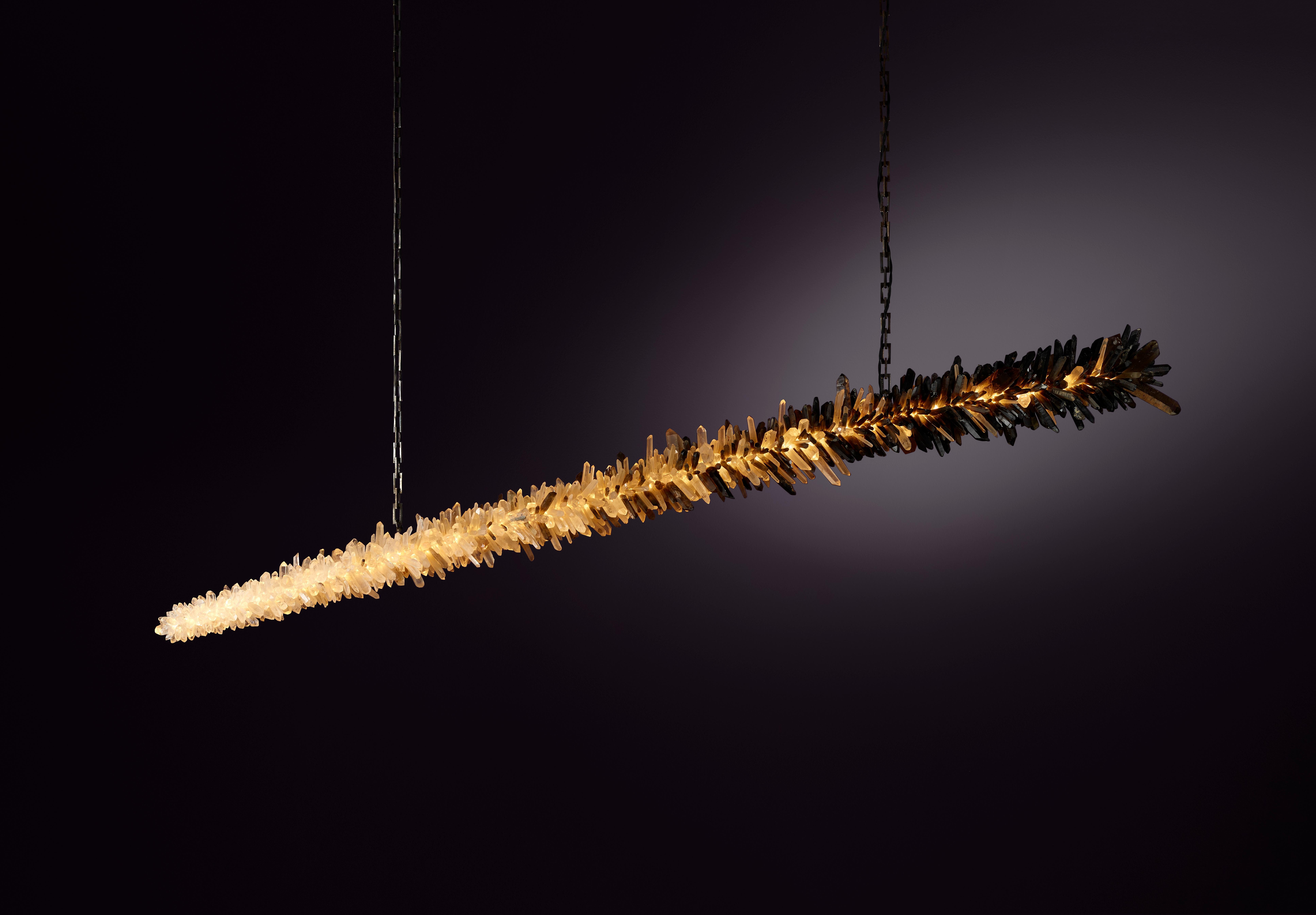 Lampada a sospensione Meteor 210 di Christopher Boots
Dimensioni: D 25 x L 210 x H 25 cm.
Materiali: Cristalli di quarzo chiaro naturalmente non tagliati, cristalli di quarzo fumé naturalmente non tagliati, ottone invecchiato.

Disponibile in 90 cm,