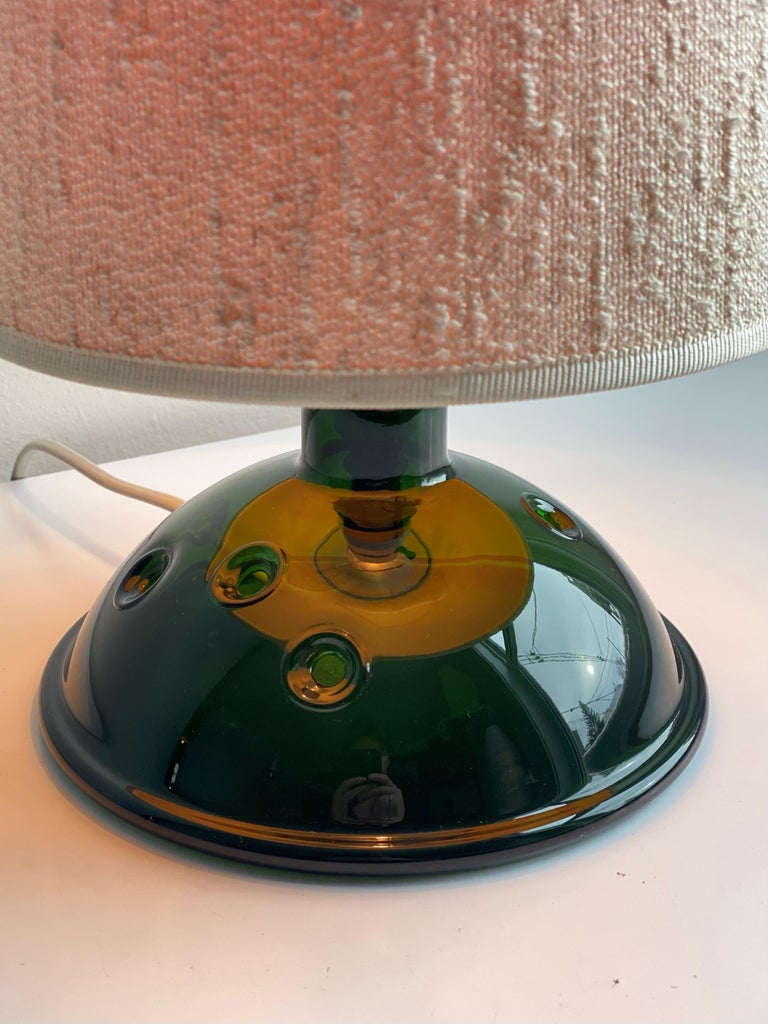 Small table lamp with rarely seen original linen shade and dark green blown glass base, part of the Meteor collection due to its perforations in the glass. Designed by Michael Bang for Holmegaard. Made in Denmark, 1970’s. In good vintage condition,