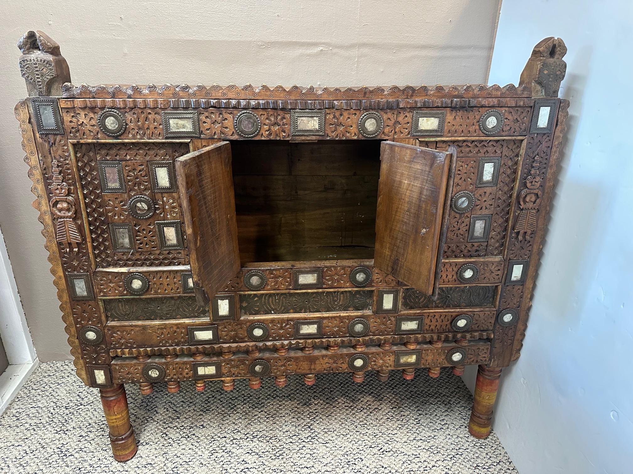Antiguo armario nupcial indio Damachiya tallado a mano, con meticulosa decoración e incrustaciones de espejos, formas figuradas y animales.  Un par de pequeñas puertas se abren en el centro para dejar espacio de almacenamiento para mantas, sábanas y