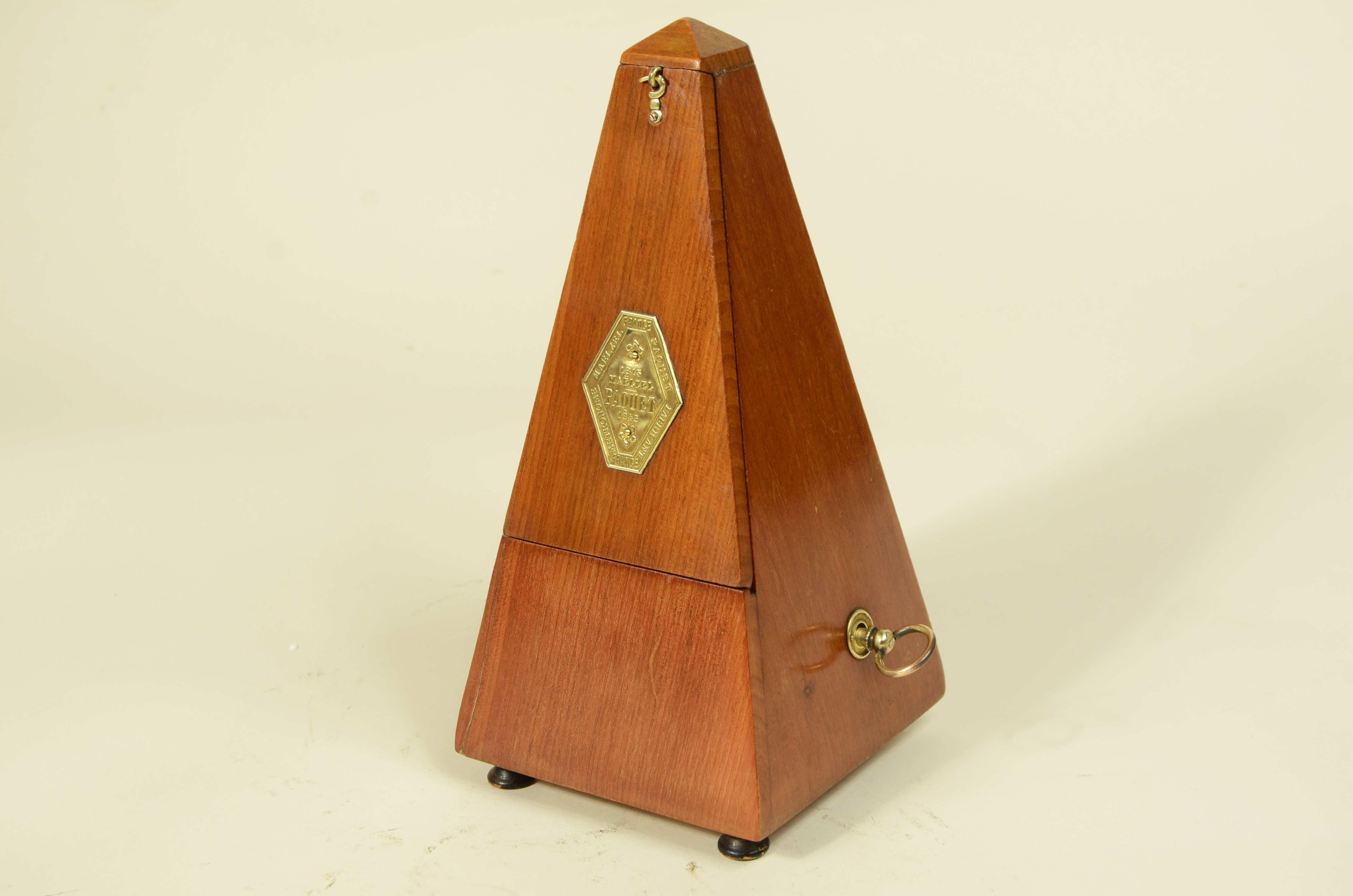 Metronomo sistema Paquet 1815 e Johan Maelzel 1846 della seconda metà del XIX secolo. 
Misure cm 11x11x23,5 – 4.3x4.3x9.3.
L'ultima foto è la confezione regalo.
Si tratta di uno strumento in legno di rovere utilizzato per misurare il tempo della