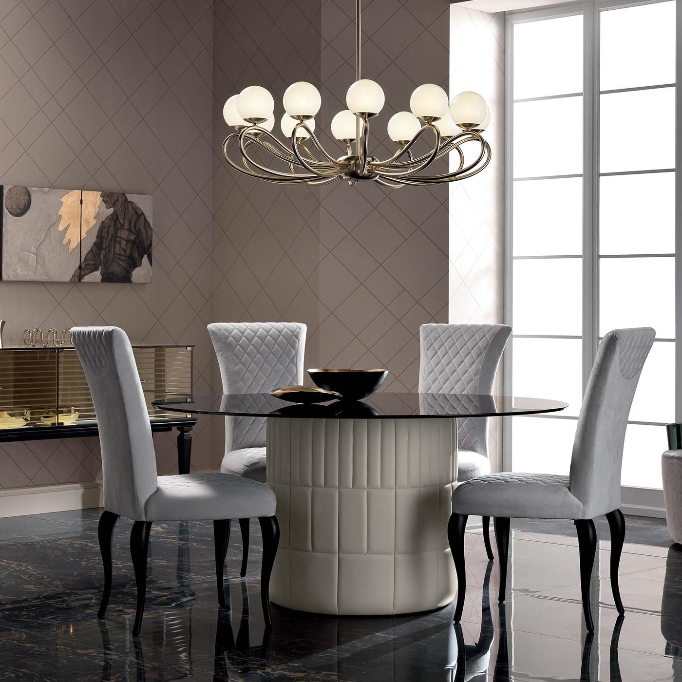 Designed by by Marzia and Leo Dainelli for Veblen, this round table displays Classic appeal and timeless elegance that will elevate any dining room interior. This exquisite piece features a back-lacquered, tempered glass top with smoked finish and