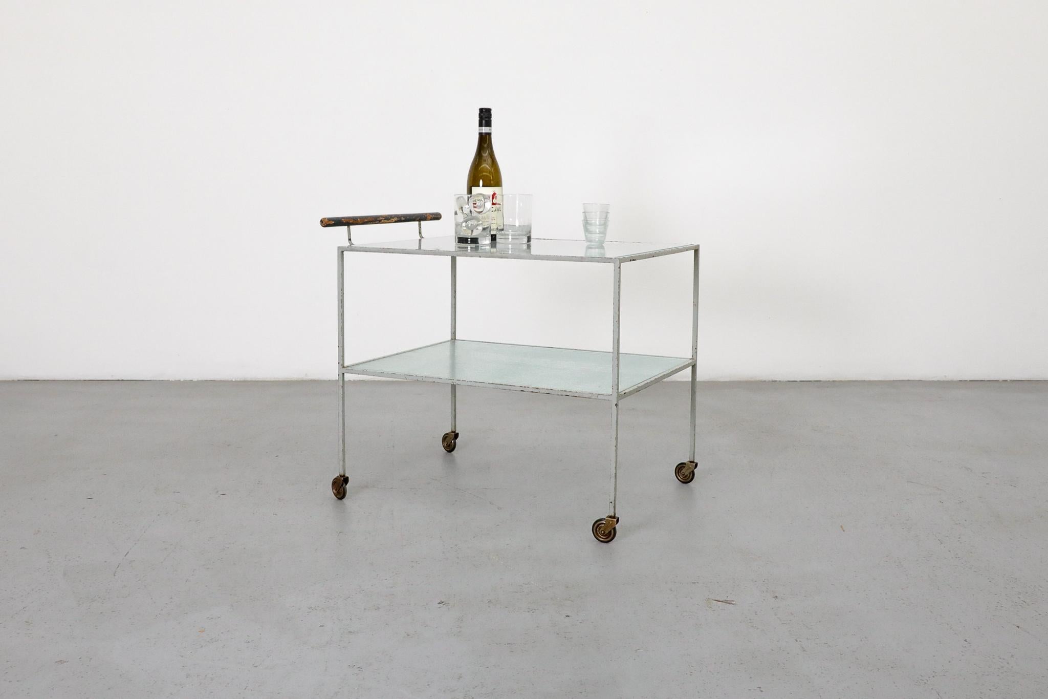 Un élégant et fonctionnel chariot de bar de style Bauhaus attribué à Metz & Co, Pays-Bas, vers 1935. Ce chariot à deux niveaux présente un cadre original en métal émaillé gris pâle avec une poignée en bois peint et des roues pivotantes à 360 degrés