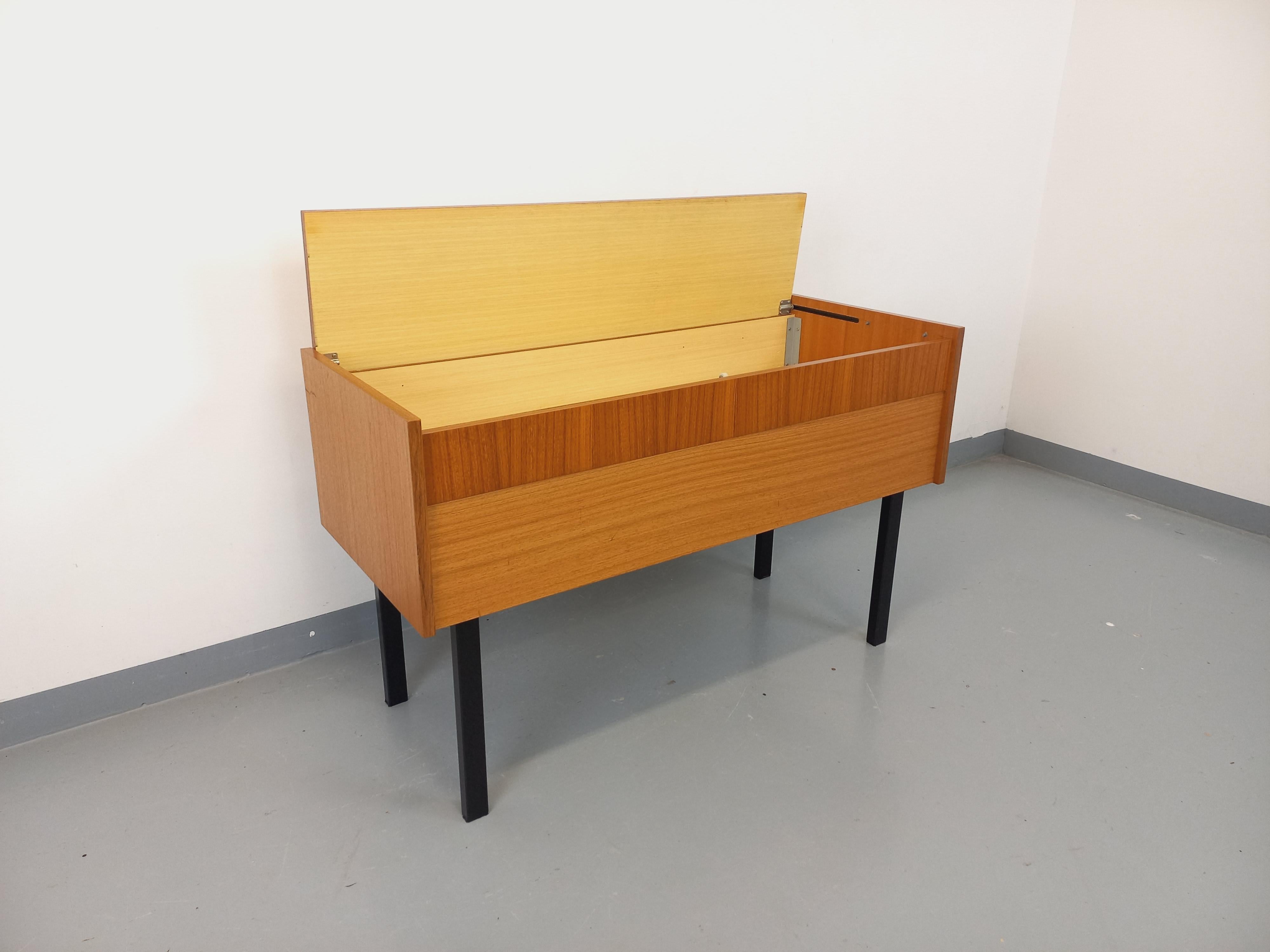 Meuble de rangement / coffre sur pieds vintage des années 60, type petite enfilade ou console, style moderniste, en teck, pieds tubulaires carrés en métal noir, plateau supérieur coulissant donnant accès à un grand espacede rangement, bon état