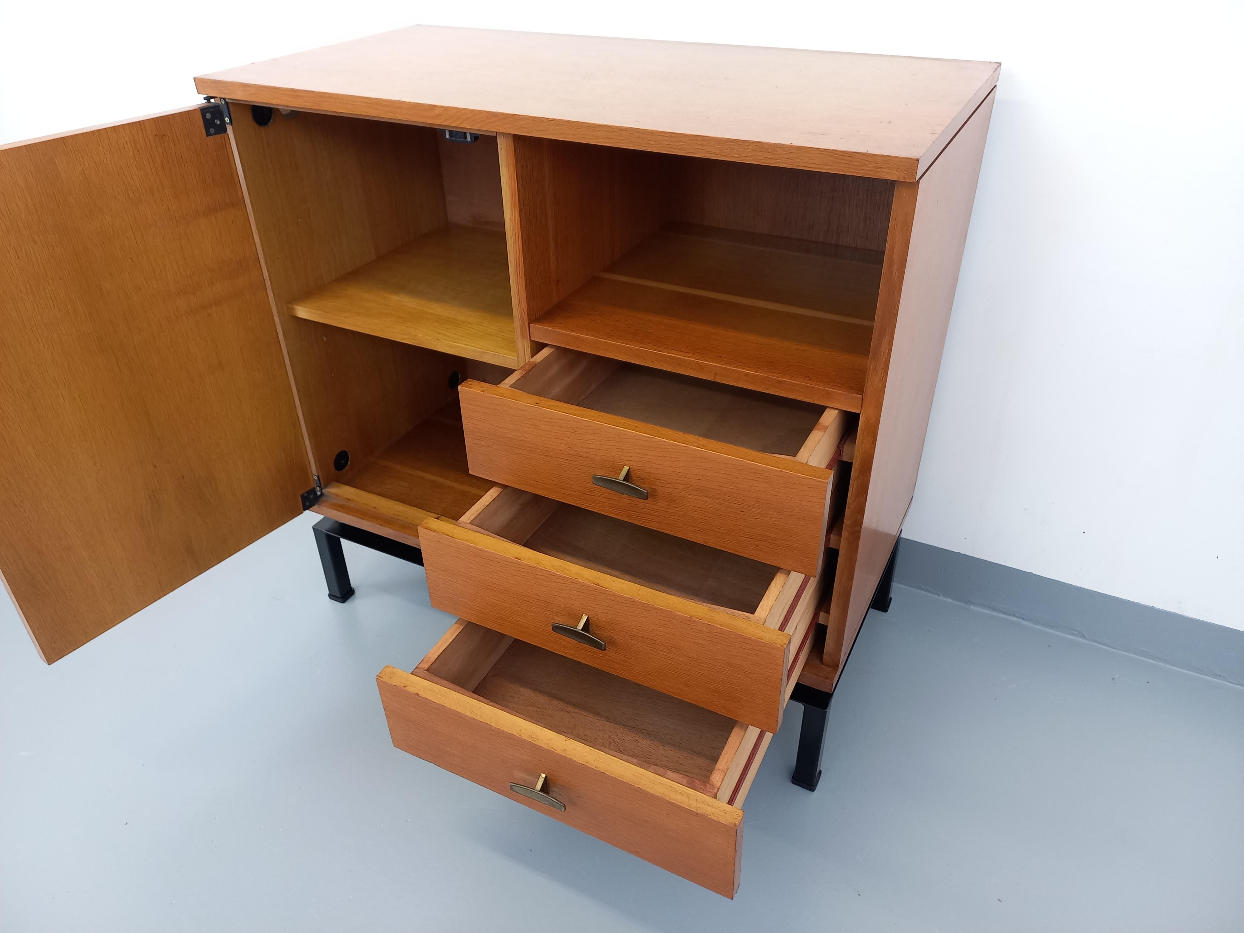 Meuble de rangement vintage style moderniste des années 50, par Marcel Gascoin pour les éditions françaises Alveole (étiquette présente), en bois de chêne, poignées laiton, piétement en métal noir. Beaucoup de rangements : 1 niche ouverte, 1 porte