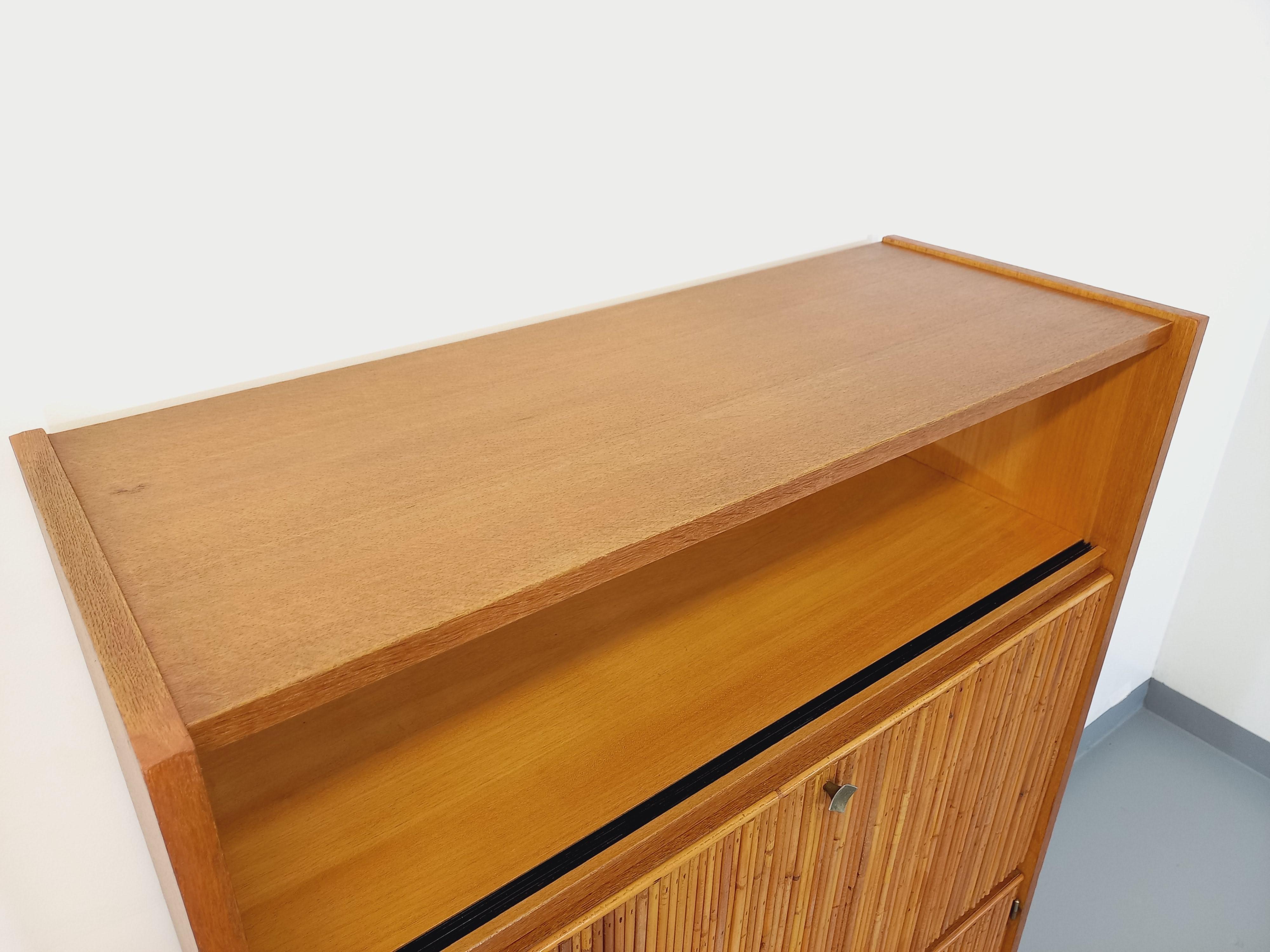 Meuble secrétaire vintage des années 60, en rotin et bois de hêtre clair. Beaucoup de rangements : 1 niche ouverte, 1 partie secrétaire/bureau, 2 portes en partie basse avec une étagère intérieure, ravissantes petites poignées losanges en laiton,