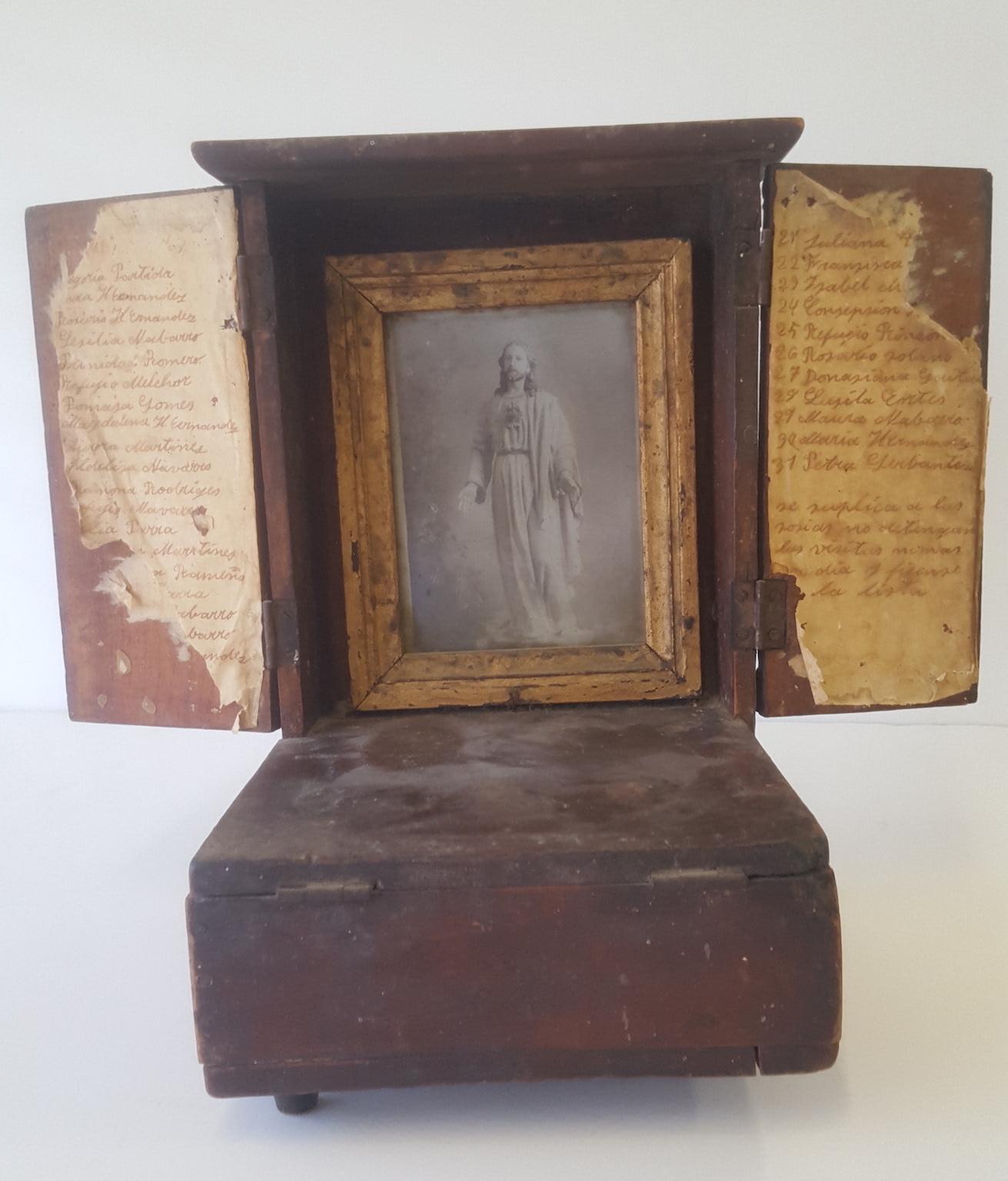A small wooden altar with a framed guilt framed print of Christ used for personal devotion and an interior locked coin box for offerings.