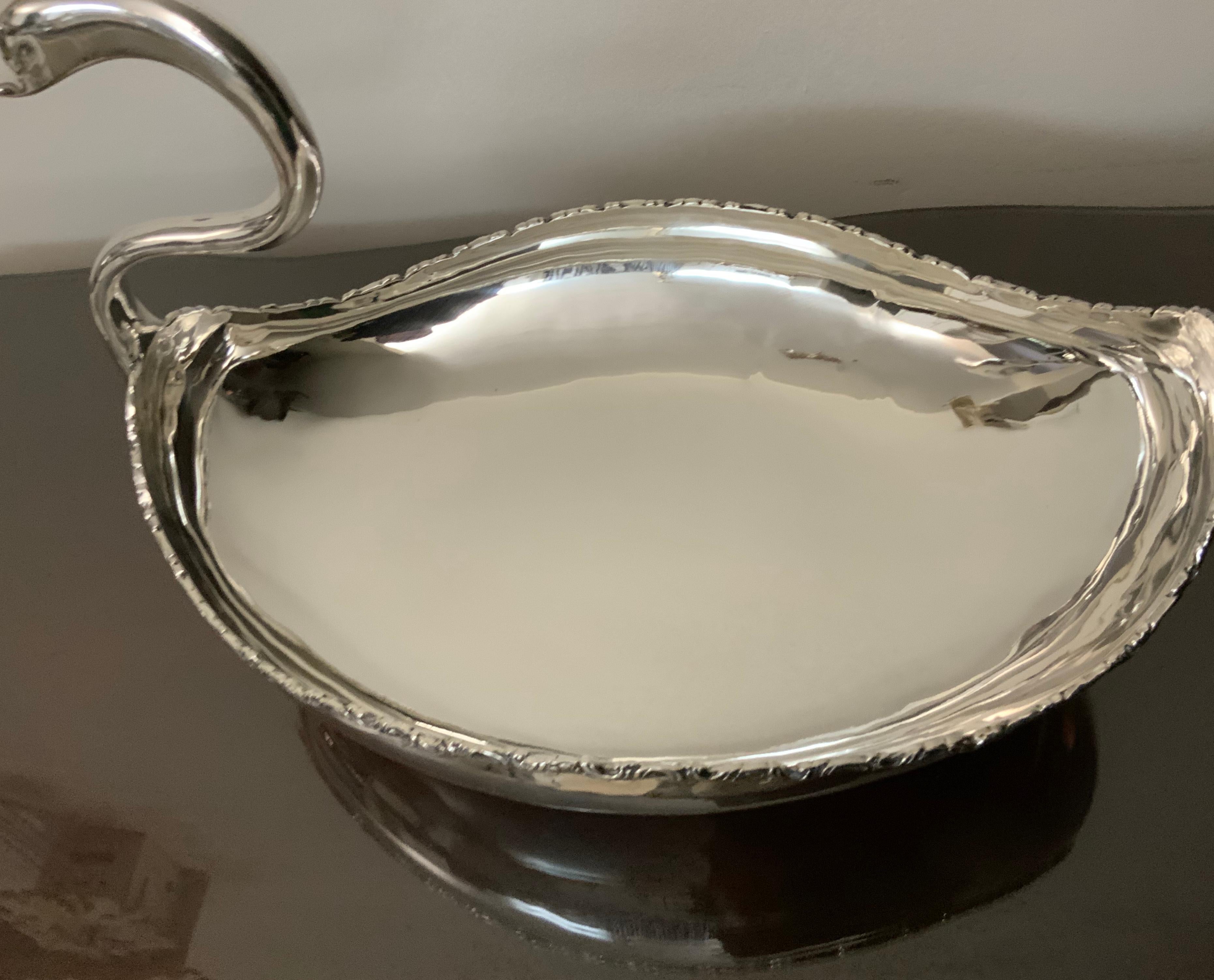 A silver swan bowl centerpiece that has a long stylized neck and its bowl body is decorated with a garland of repousse scrolls. The centerpiece sits in an attached oval base. The piece is heavily stamped in the lateral aspect of the body with the