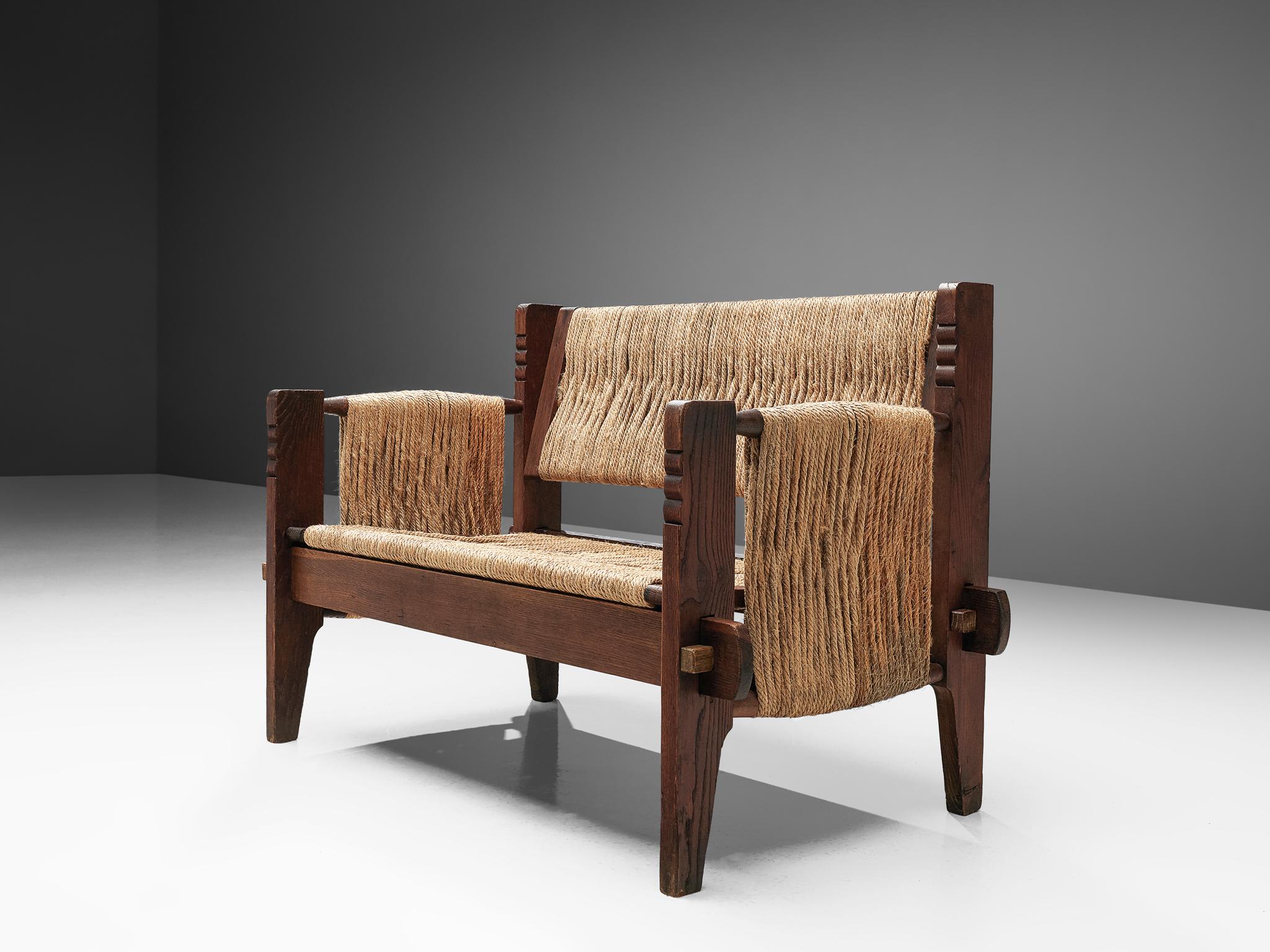 Bench, oak and rope, Mexico, 1950s

This robust Mexican settee originates from the 1950s. The frame is made of stained oak with decorative carved elements. The seat and legs are attached by wooden wedges. The seat, back and armrests are made of