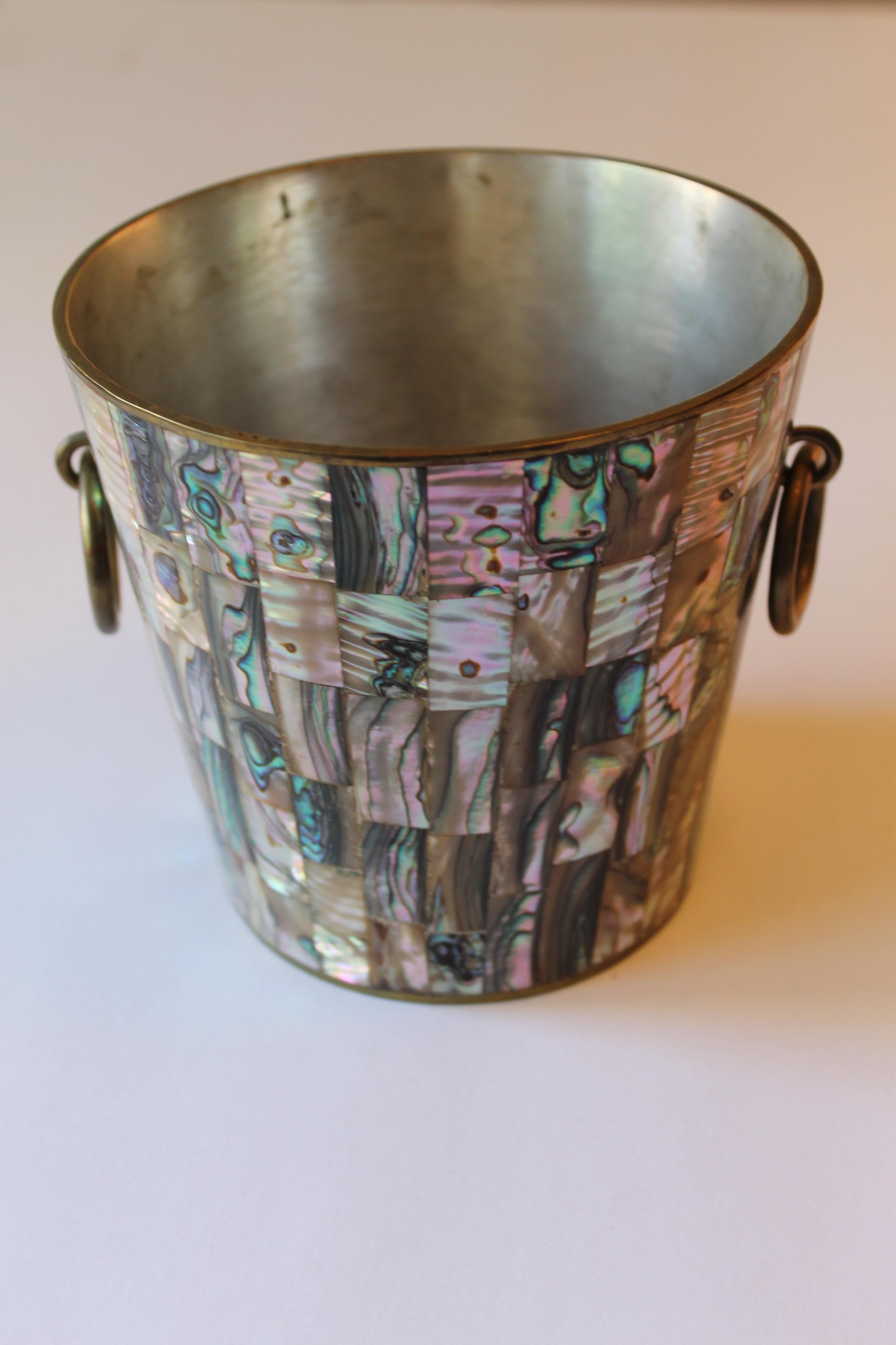 A small solid brass ice bucket from Taxco, Mexico, entirely covered in colorful abalone shell tile overlay. Interior washed in silver. Marked METALES TAXCO, HECHO EN MEXICO. No missing abalone shell pieces. Measures: 5.25