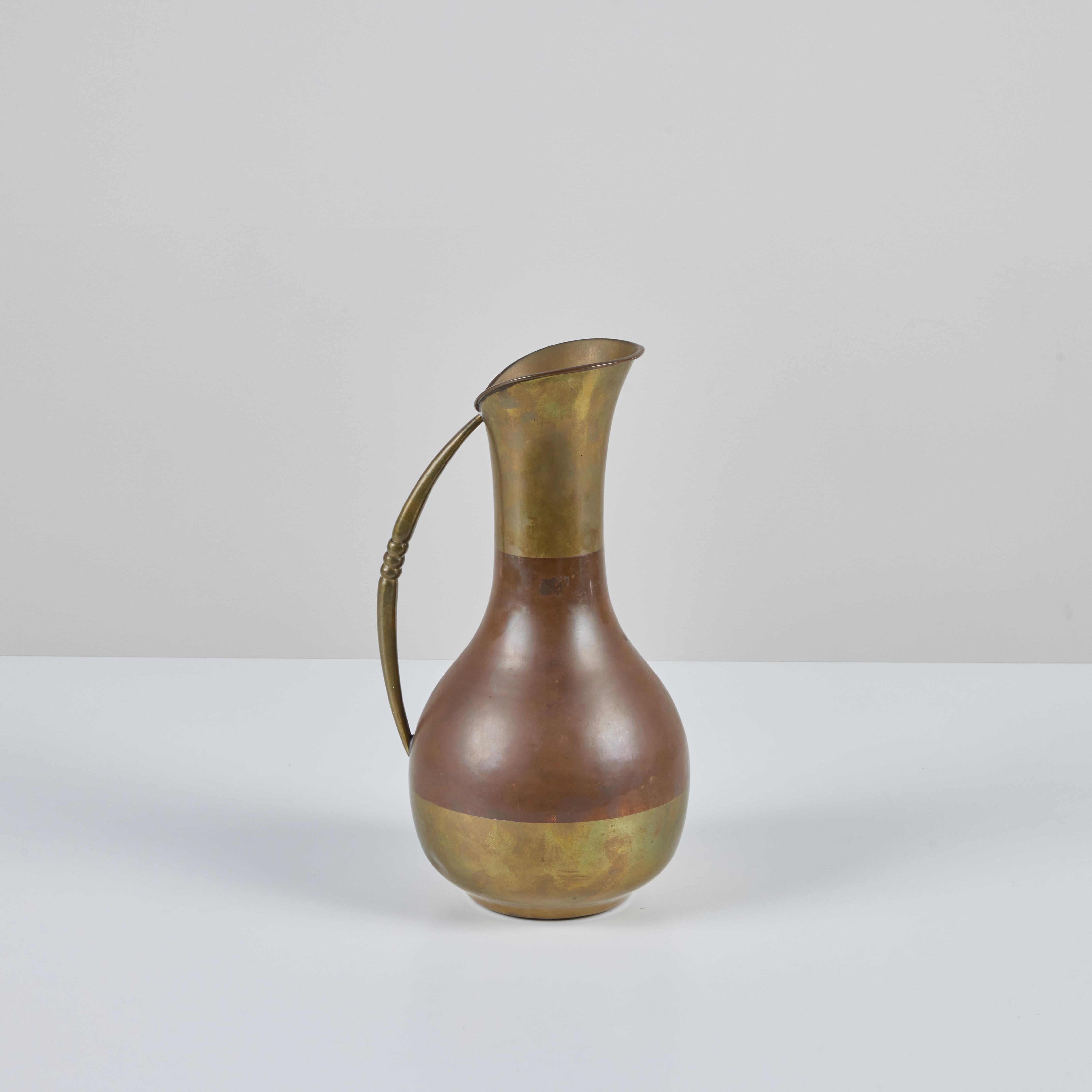 Brass and copper pitcher made in Mexico. The pitcher features a fluted opening with a copper middle section and brass top, bottom and handle. The handle has a simplistic three ribbed detail.
Stamped 