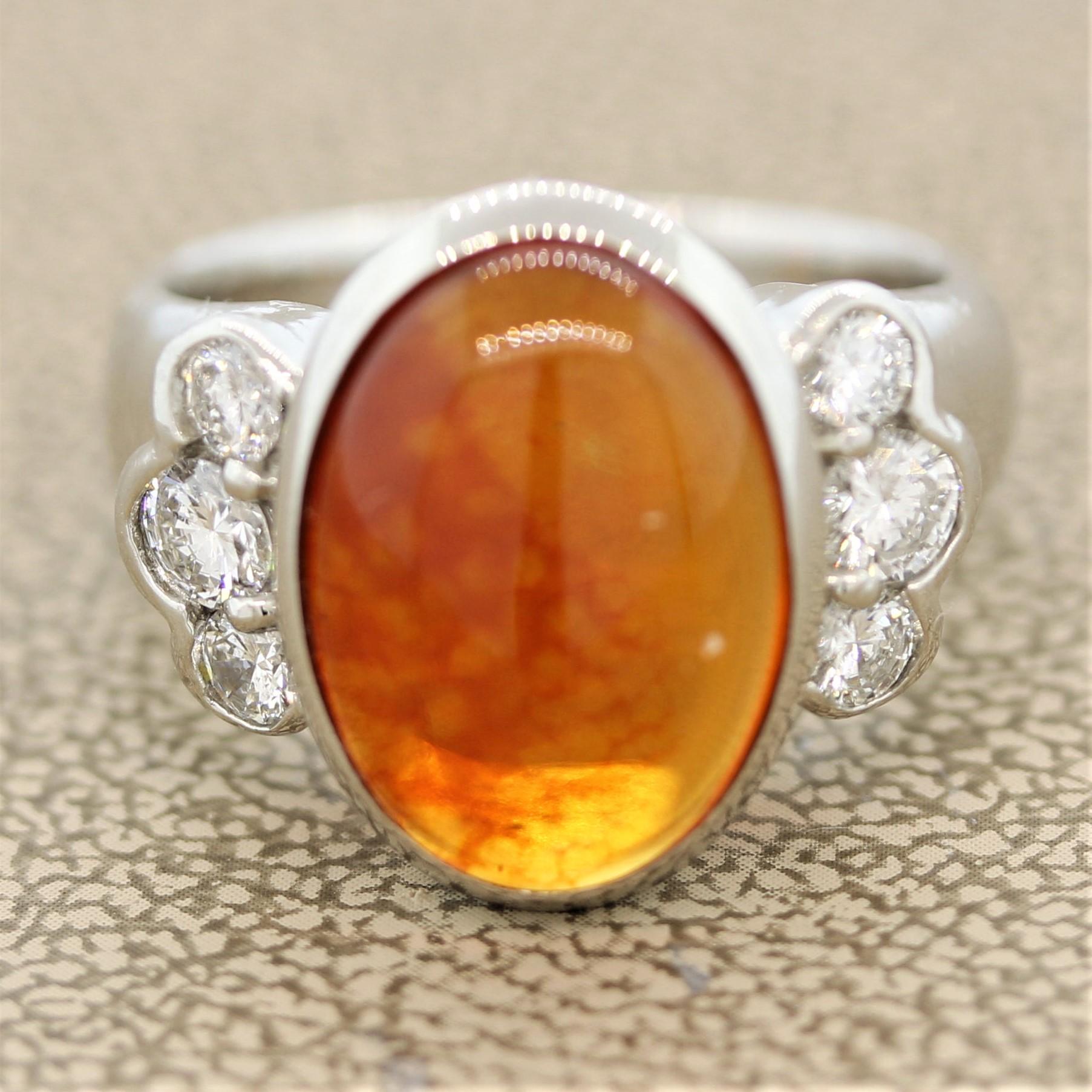 A deep royal jelly colored Mexican fire opal! It weighs 15.3 carats with a juicy orange color and shows play of color with light flashes of green and blue. It is accented by 6 round brilliant cut diamonds set in the sides of the opal and weigh a