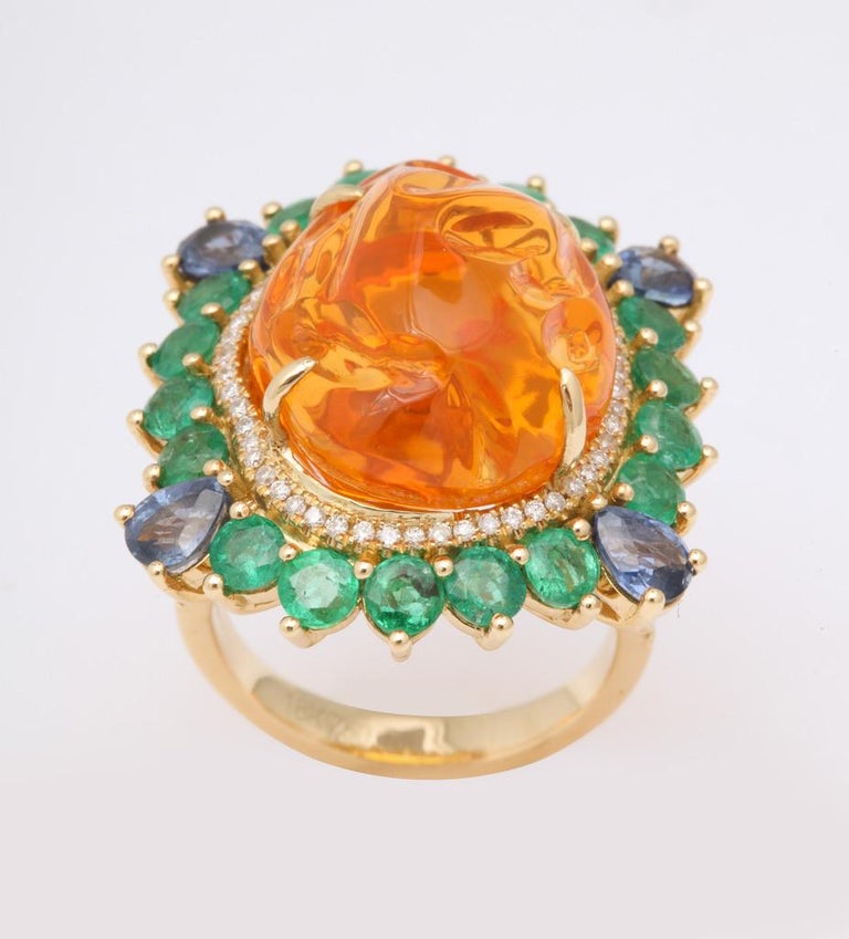 A bright orange, baroque shaped cabochon Mexican fire opal is framed in emeralds, sapphires and diamonds creating an exceptional burst of color.  A completely one of a kind cocktail ring.
Mexican fire opal: app 16 carats
Emeralds: app 2 1/2