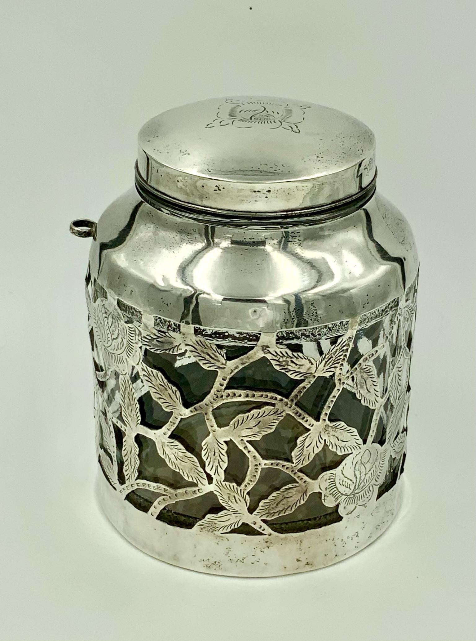 Jarre vintage mexicaine en verre à décor floral gravé avec porte-cuillère. Cette magnifique jarre a été fabriquée au Mexique et présente un magnifique manchon en argent avec un motif floral gravé. Les manchons enveloppent un bocal en verre. La pièce