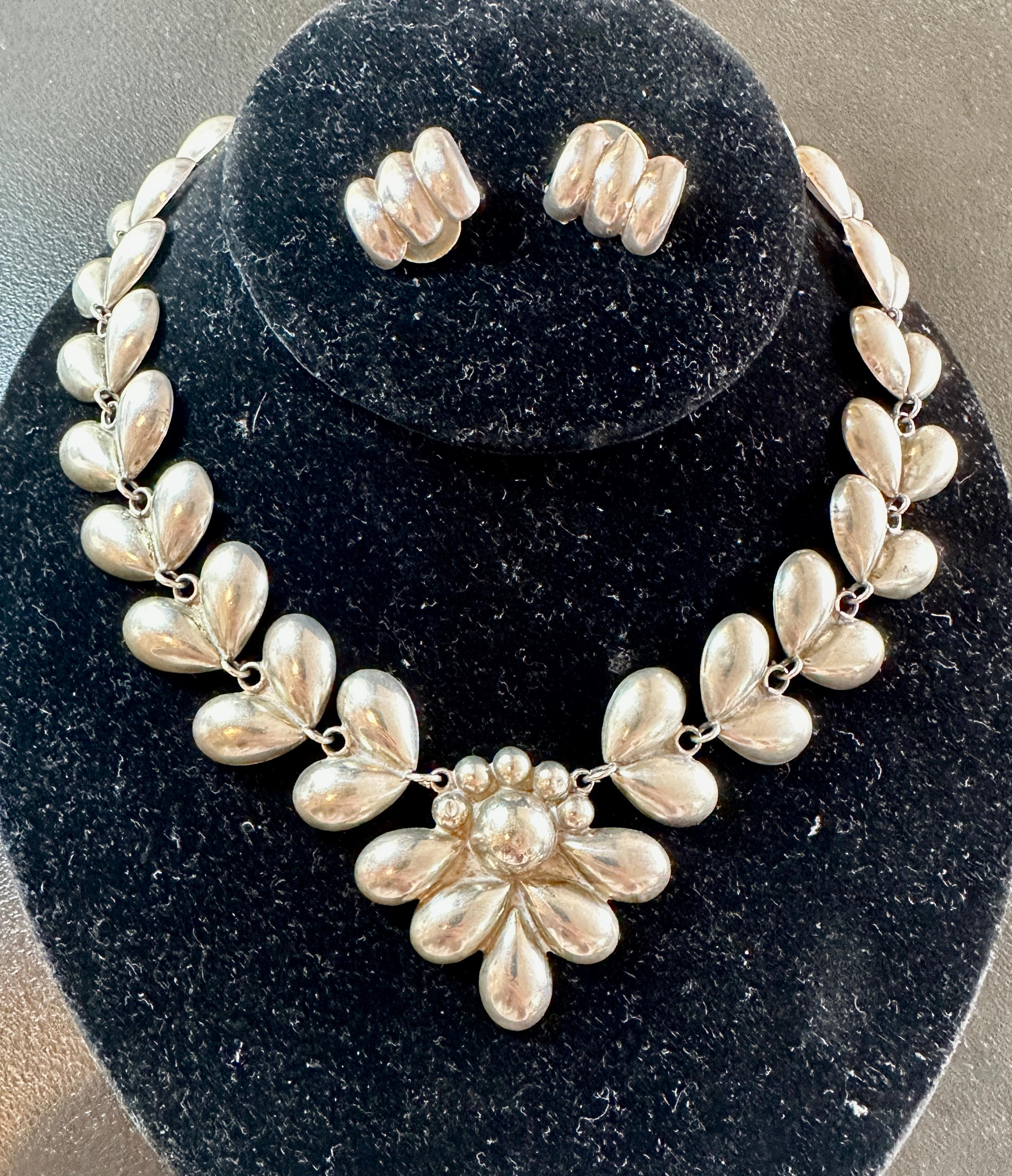 Concediti una delle più belle collane e orecchini d'argento messicani antichi Suites con motivo a cuore e fiori.  I Jewell's Mid Century Jewell's sono caratterizzati da un meraviglioso design a cuori e fiori in argento Sterling.  La combinazione tra