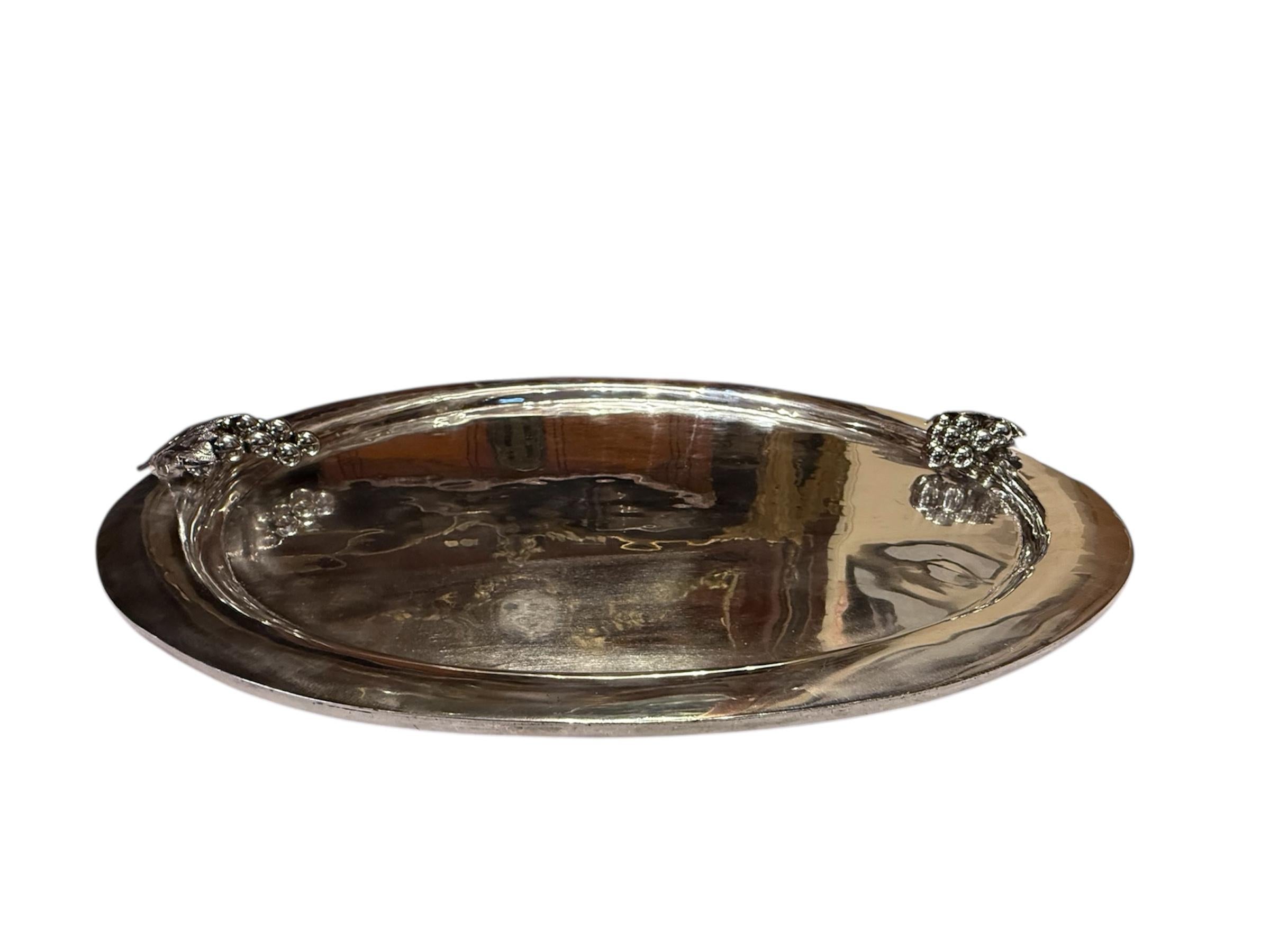 This is a Mexican Sterling Serving Tray. It depicts a large round sterling silver serving tray adorned with a bunch of grapes with leaves at each side of the tray. Below the tray is hallmarked Mexico Sterling.