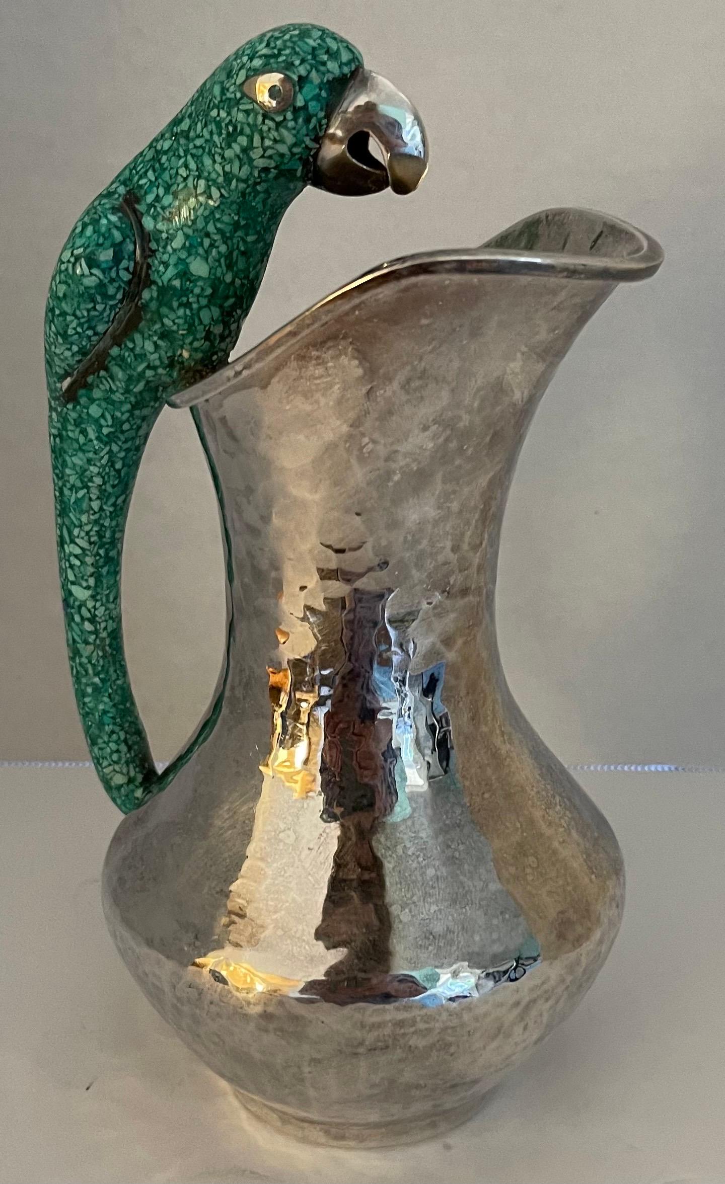 Mexican Los Castillo style parrot handle pitcher. Silver plate with lightly hammered finish and green stone parrot handle. Heavy and well made.
No makers mark or brand stamp.