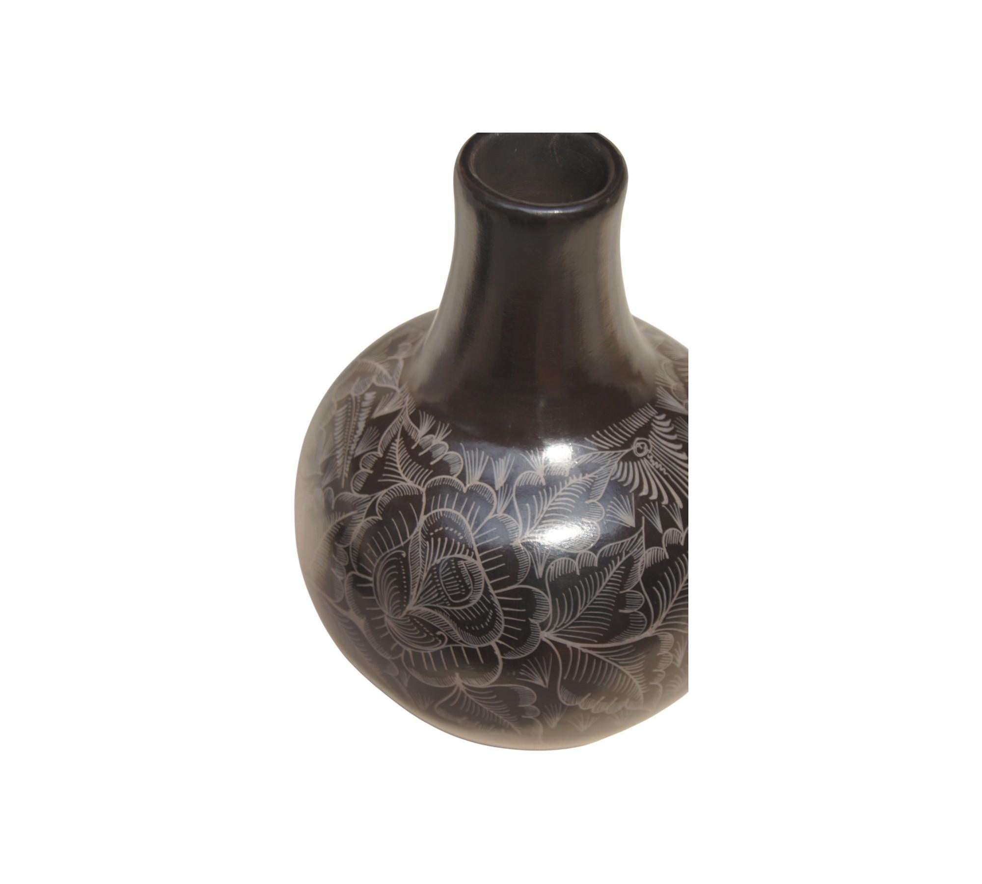 Questo squisito decanter e brocca di Huáncito, Michoacán, è un capolavoro unico nel suo genere, meticolosamente realizzato a mano in argilla nera utilizzando le tecniche tradizionali della ceramica. Le sue intricate incisioni floreali e il suo