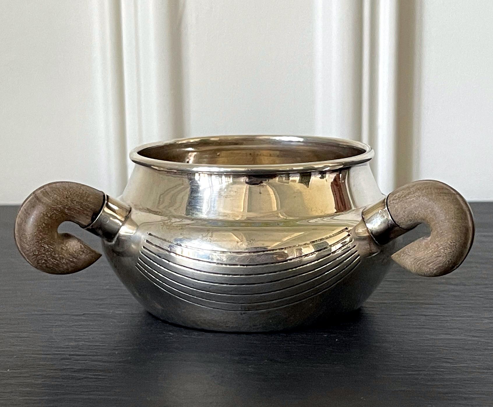 A modernist sterling silver bowl with three exotic wood handles circa 1951-1956. The bowl was designed and crafted by William Spratling in Taxco Mexico. Its bulbous form is accentuated with three curled wood handles. The surface was decorated with