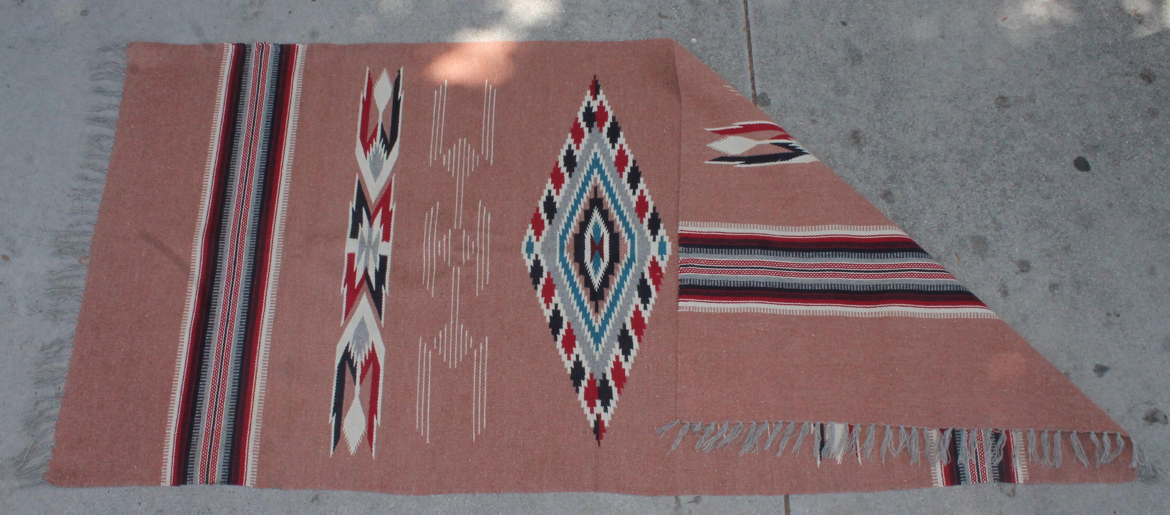 This fine Mexican weaving is in pristine condition and retains the original fringe. It’s a wonderful salmon color withe the seeing eye pattern in the middle of the weaving.