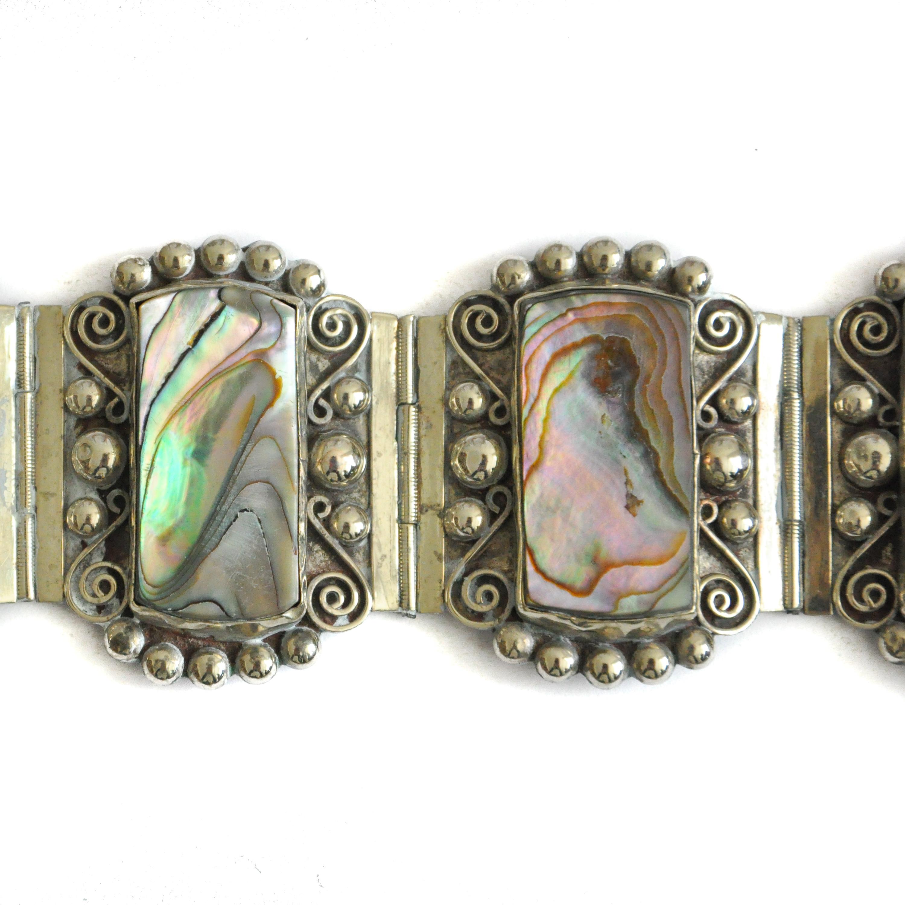 A beautiful mid-century Mexican bracelet comprised of fine sterling silver with abalone shell. The bracelet has five decorative silver panels, with heavy beading, swirls and rectangular abalone stone mask medallion - the stone has beautiful pearl