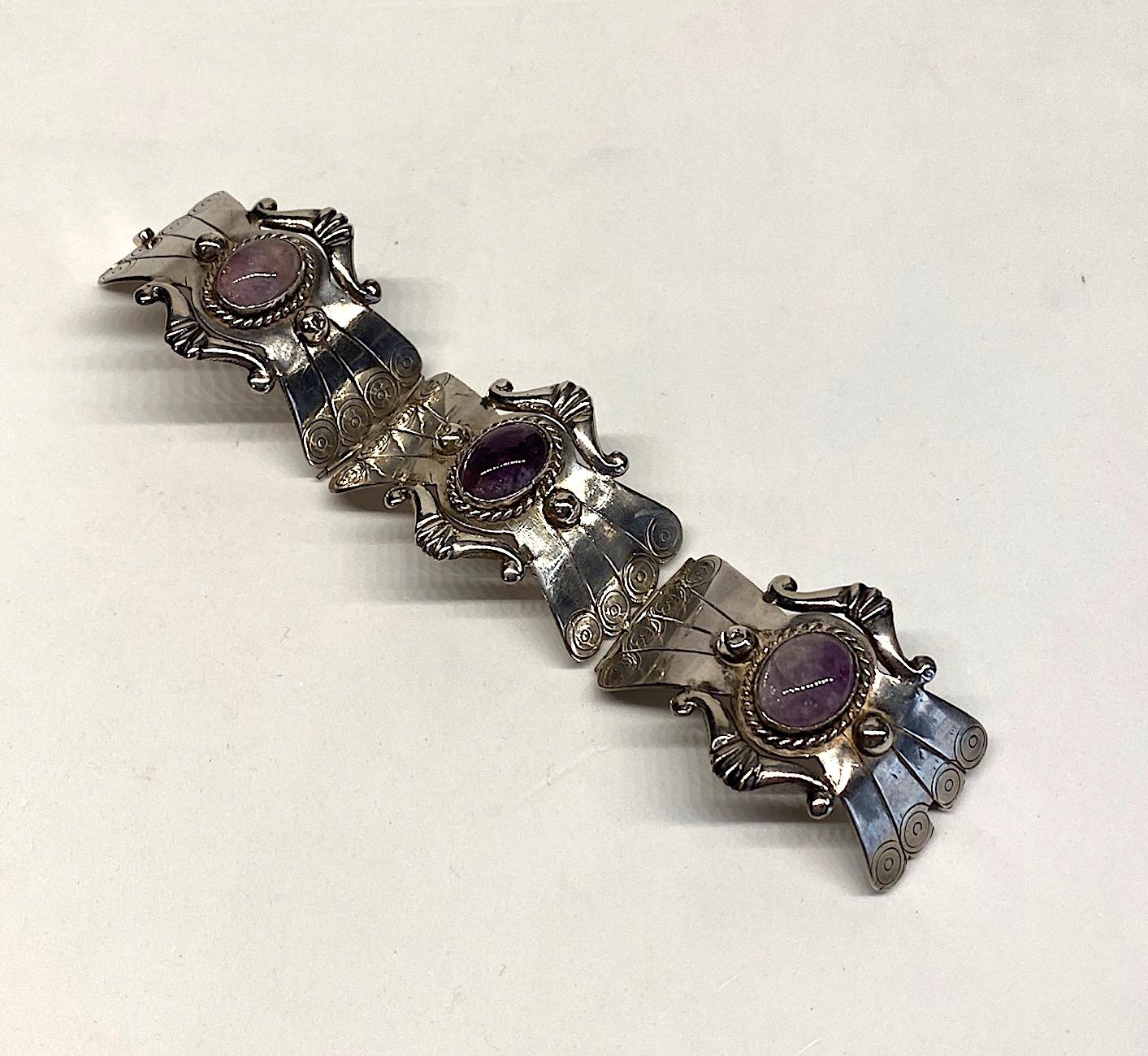 Artisan made sterling silver bracelet set with natural amethyst cabochons from the 1950s. The three curved hour glass panels are hand chased and have applied side scroll design accents and  half domes in silver. The center of each panel is bevel set