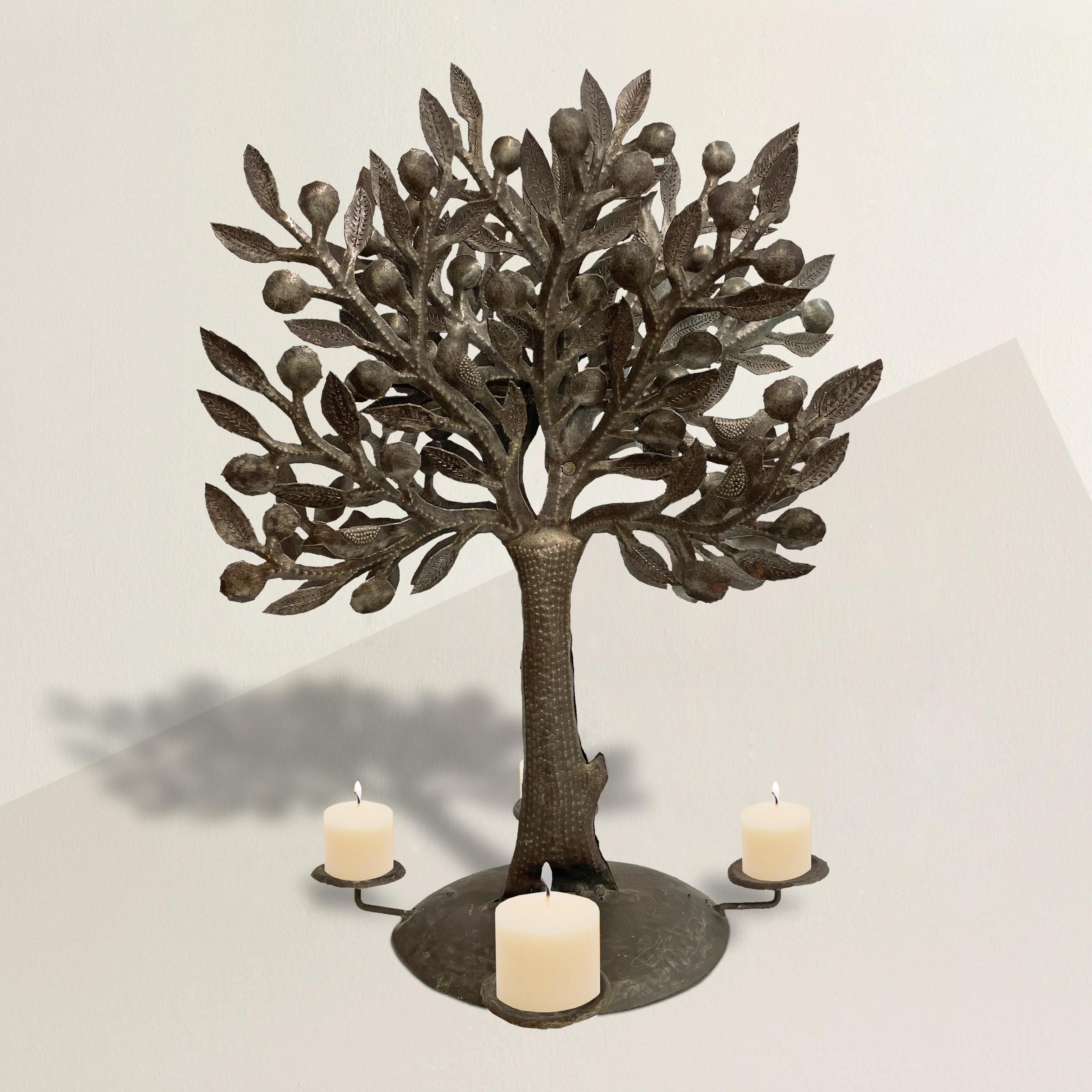 A whimsical Mexican tree-of-life candelabra constructed from several sheets of steel, hand-cut and punched with leaves, birds, and berries, and supported by a tree trunk that's surrounded by four candle cups.