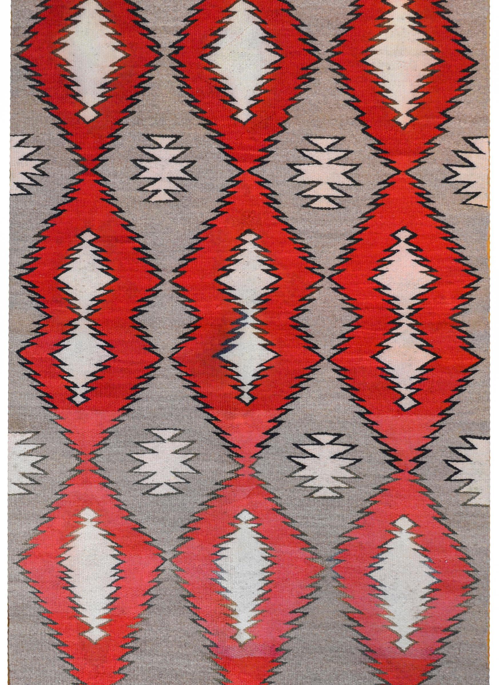 A mesmerizing early 20th century Navajo rug with an all-over pattern woven of abrash crimson and gray diamonds with zigzag edges giving a dizzying appearance.