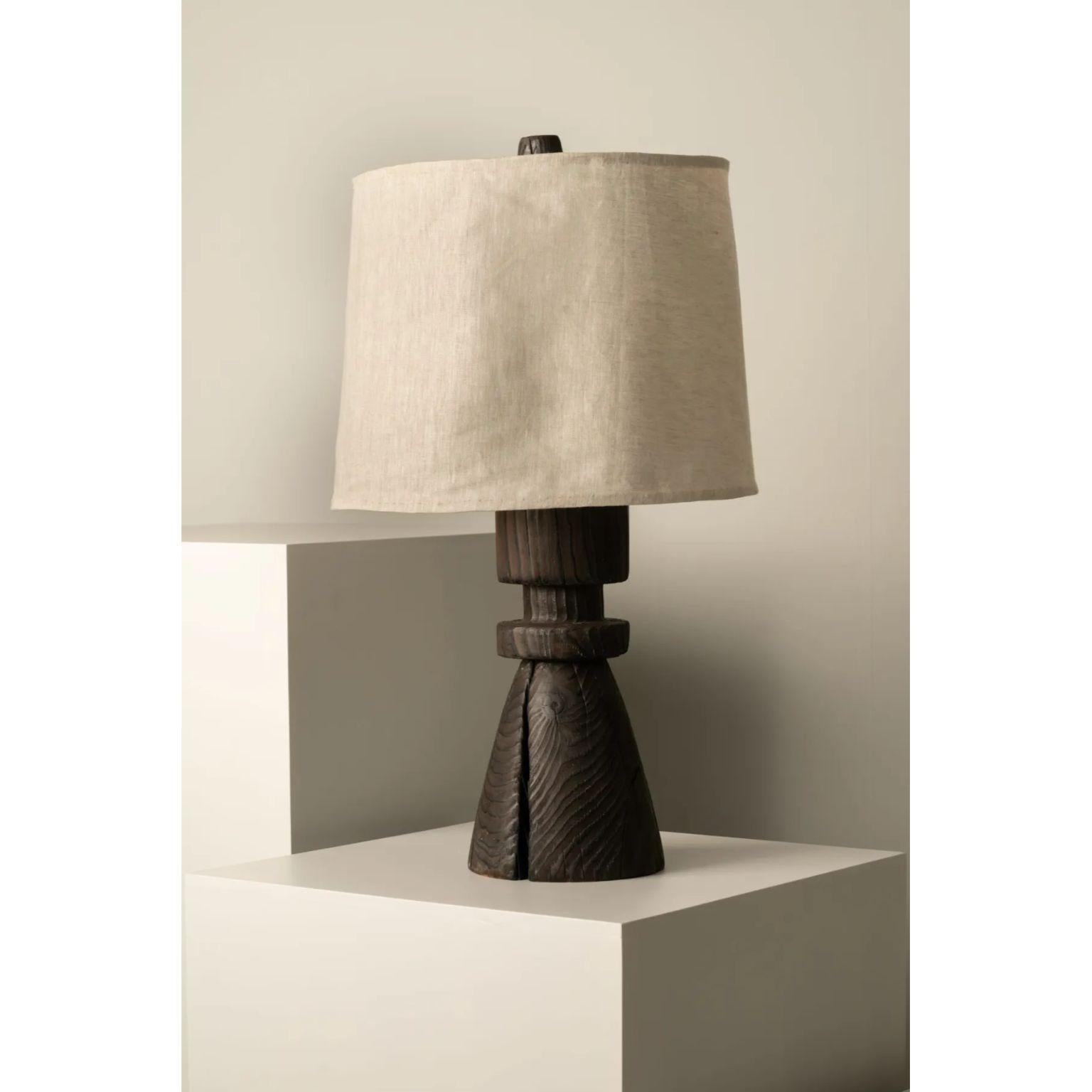 Mezquite Table Lamp by Isabel Moncada
Dimensions: Ø35.5 x H 68.5 cm.
Materials: Linen and pine wood.

When burnt using the Japanese technique Shou sugi ban, the wood grains become apparent and cracks appear randomly in the solid trunk. Hence,