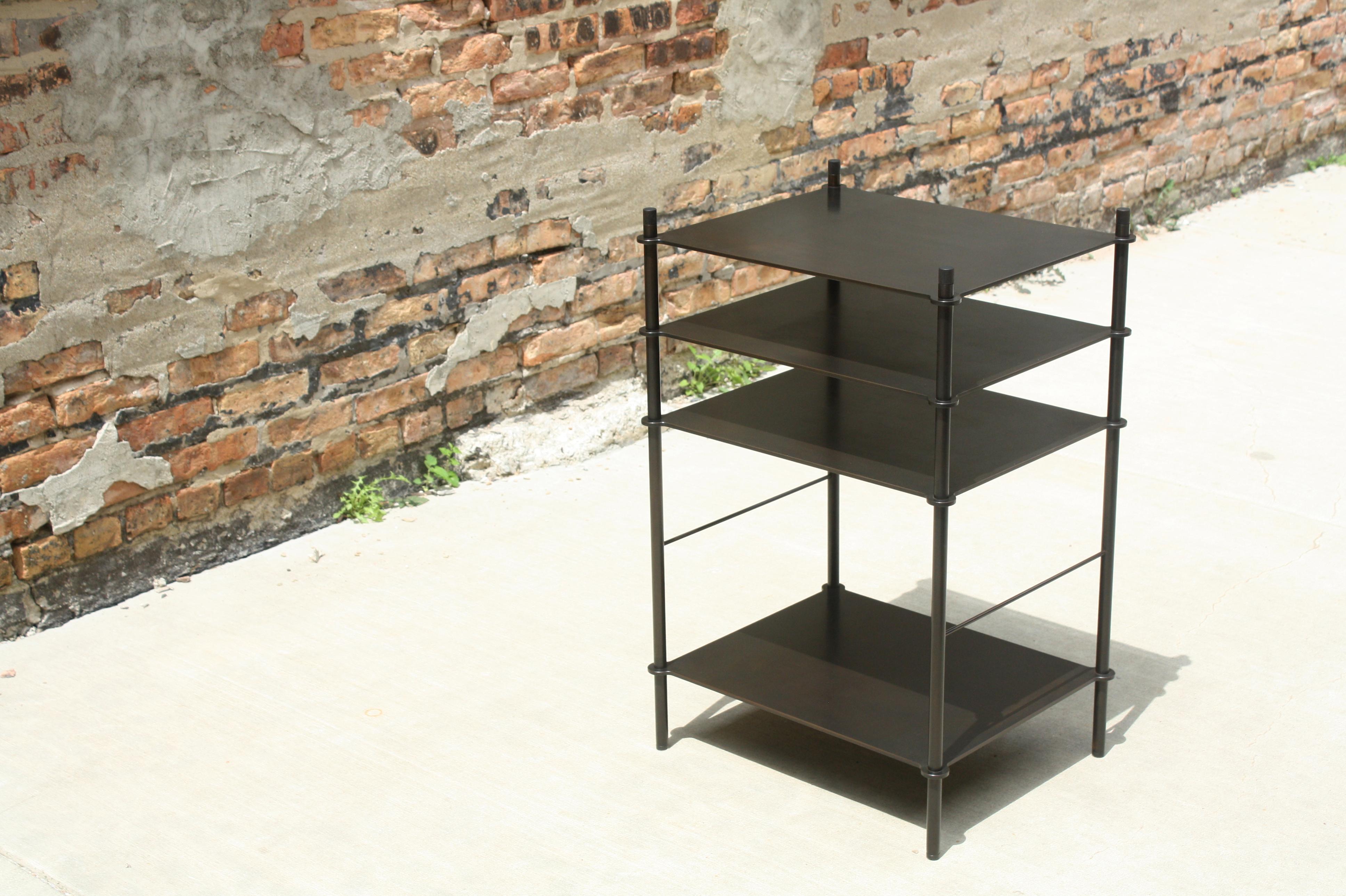 Tiered surfaces are precision welded to leveling legs creating an open shelving system that can be customized for any space or use. Shown in acid blackened steel with hand-turned and ebonized walnut finials, the piece shown was designed to hold a