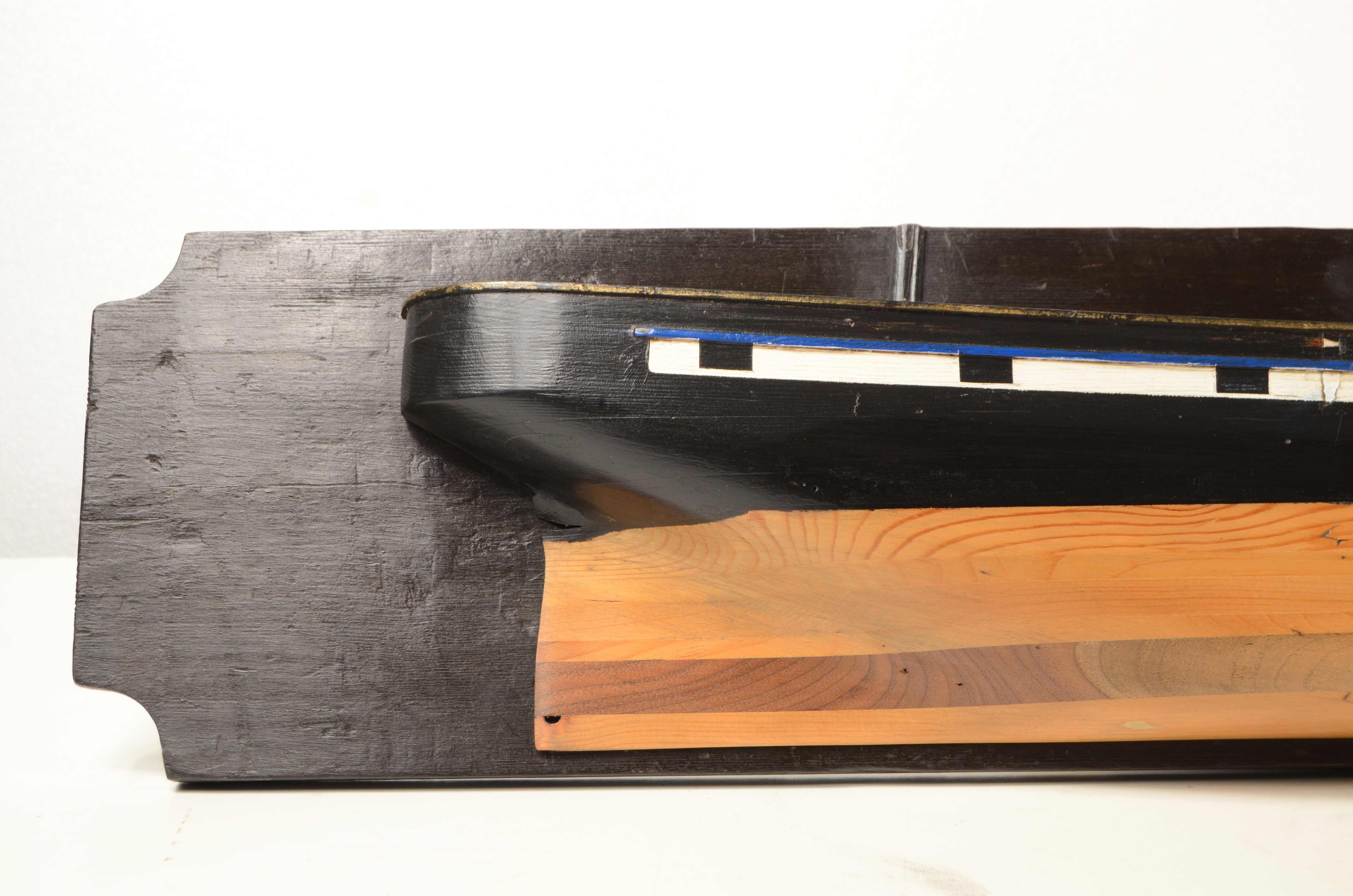 Demi-coque d'un brigantin français de la fin du XIXe siècle en bois de pin et d'acajou, montée sur une planche en bois de couleur noire, œuvre vivante de couleur noire, œuvre morte de couleur noire.
Bon état. Dimensions de la table 126x9x21.5 cm -