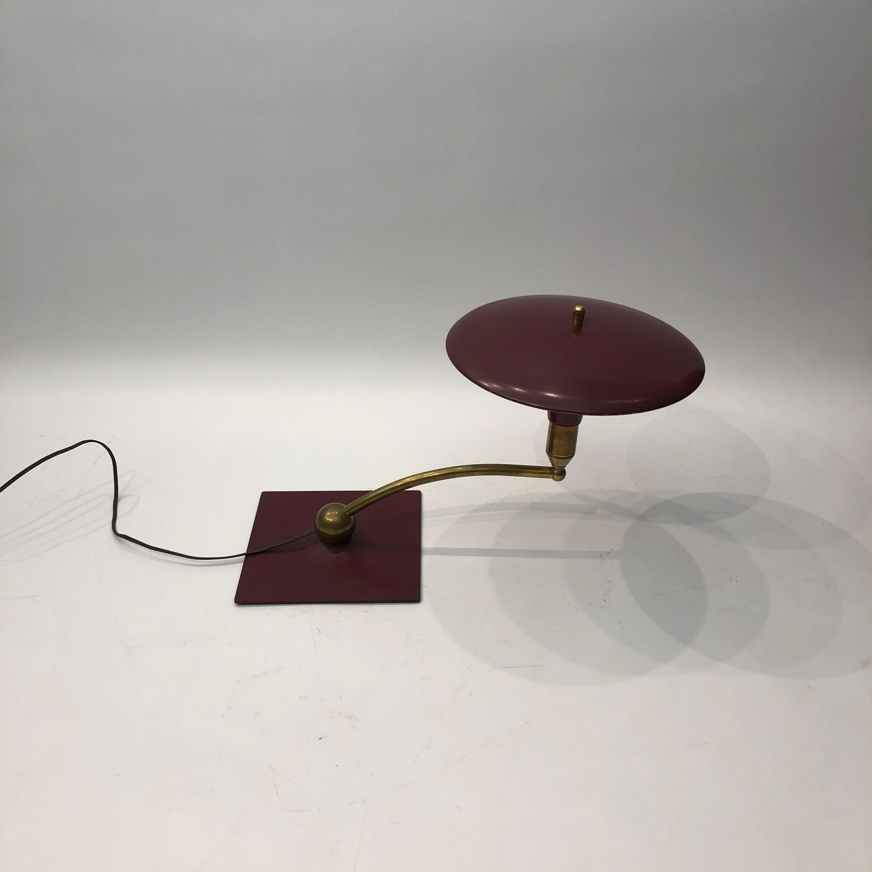 A classic desk table lamp by MG Wheeler in burgundy crackled finish and brass details. Steady heavy square base with a brass rotating ball with a curved pole that supports the UFO like shade. Elements of 1950s futurism and is evident on this classic