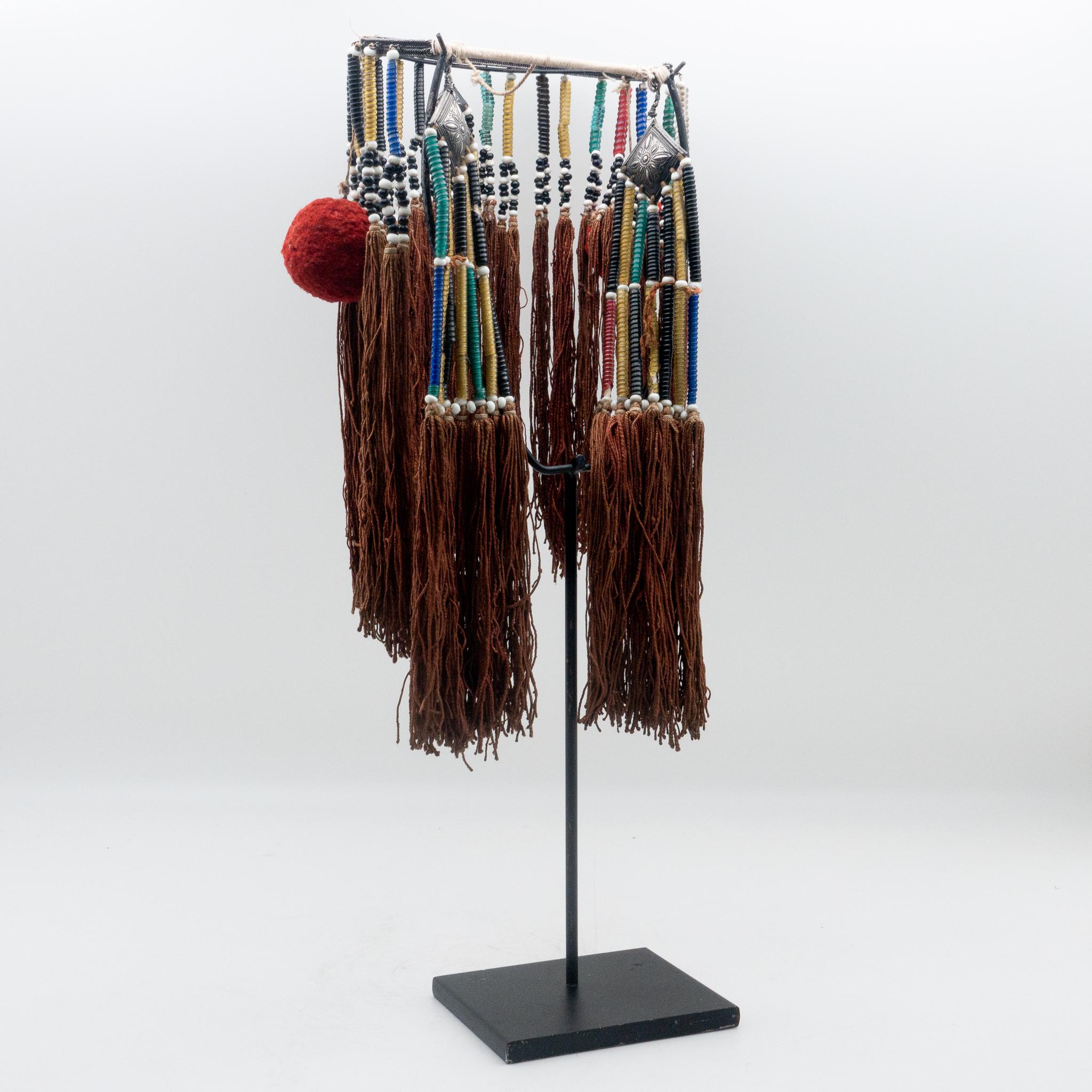 Miao Minority tribe headdress with beads, silver pendants, pom-poms, and tassels from the mid 20th century on a custom black painted metal mount.

  