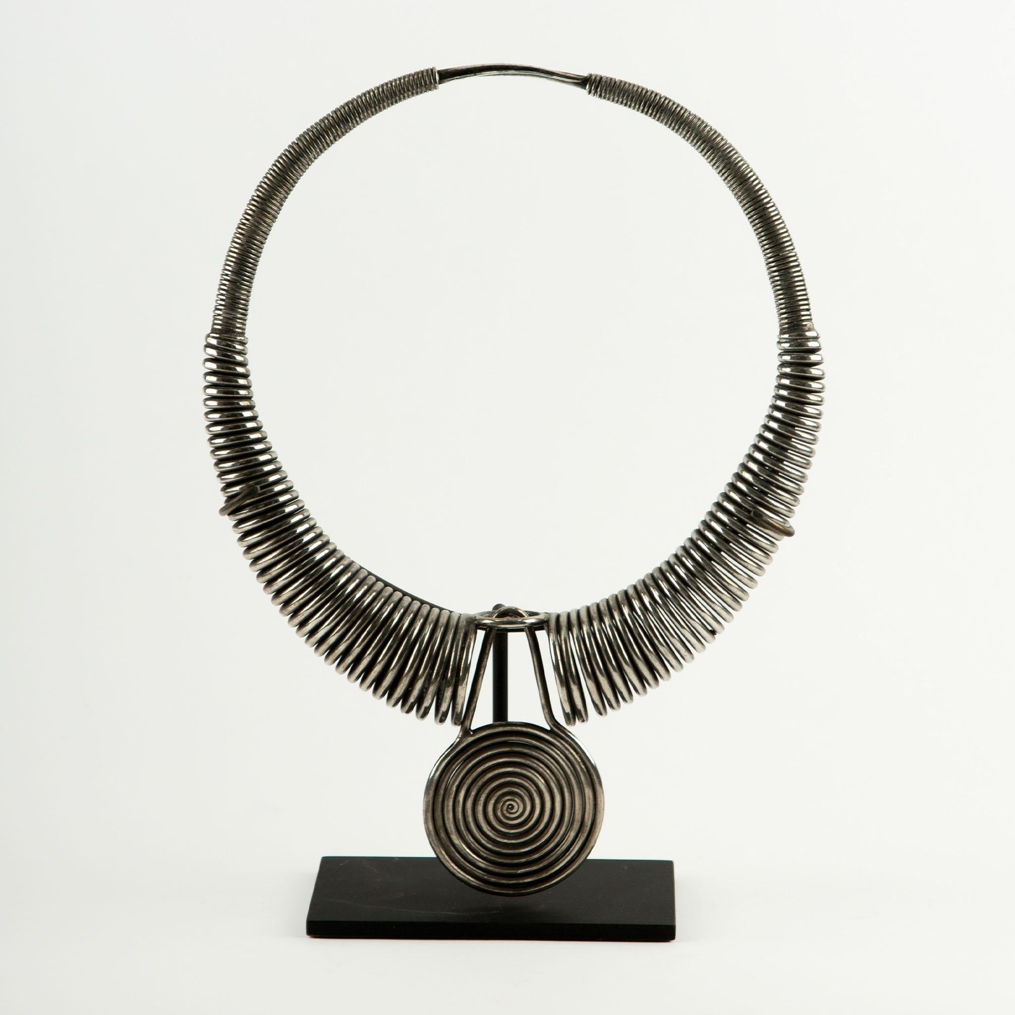 An impressive traditional Miao silver pectoral necklace, hand-forged from coiled silver wire with a large central spiral medallion. The rigid collar form is composed of thick, tightly wound wire loops, creating a bold, architectural silhouette, and