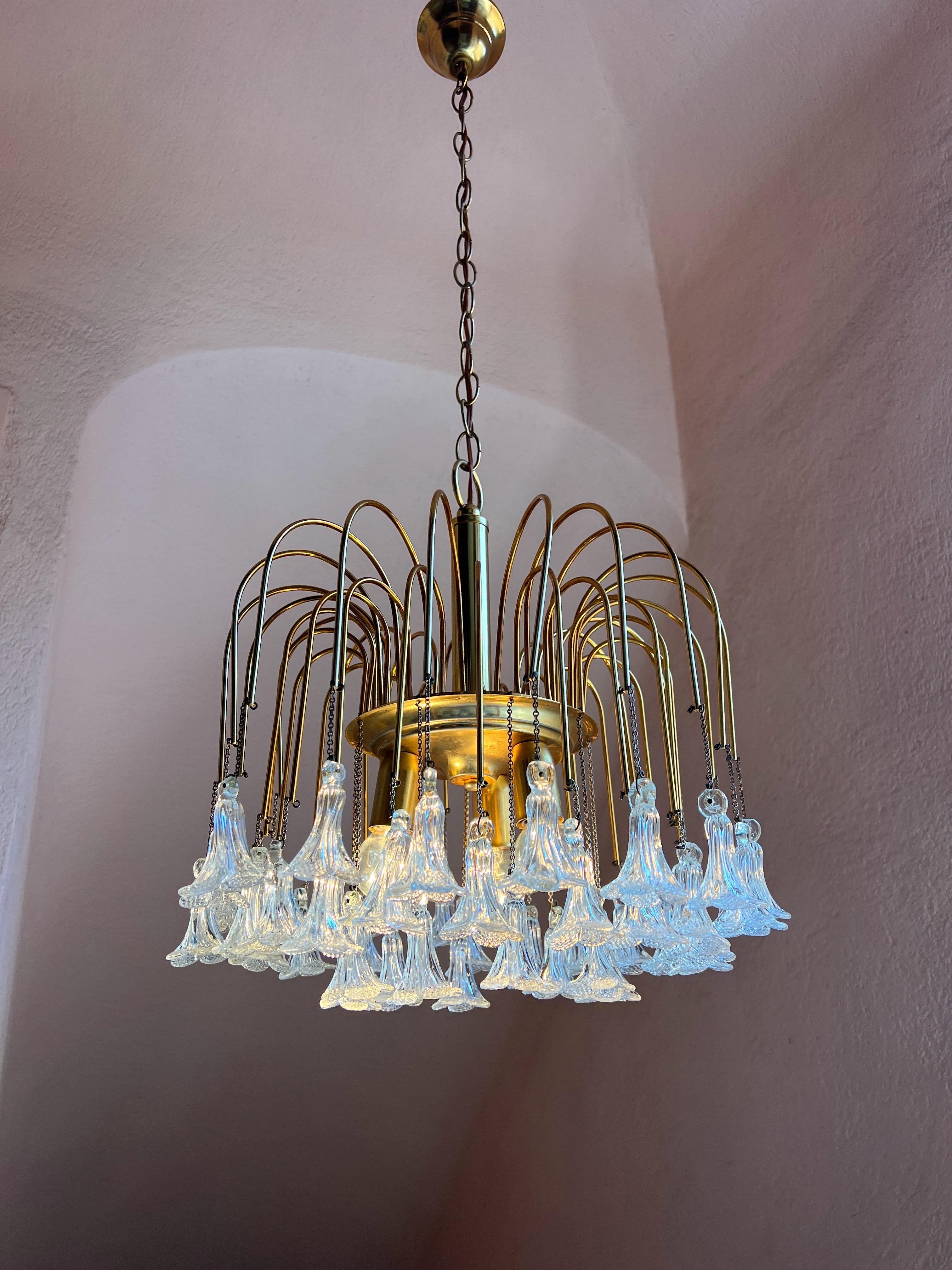 This exquisite Hollywood Regency style chandelier adorned with delicate hand blown crystal clear Murano glass flowers is a celebration of Italian craftsmanship at its finest
Each bloom sculpted in glass with masterful precision reflects the light