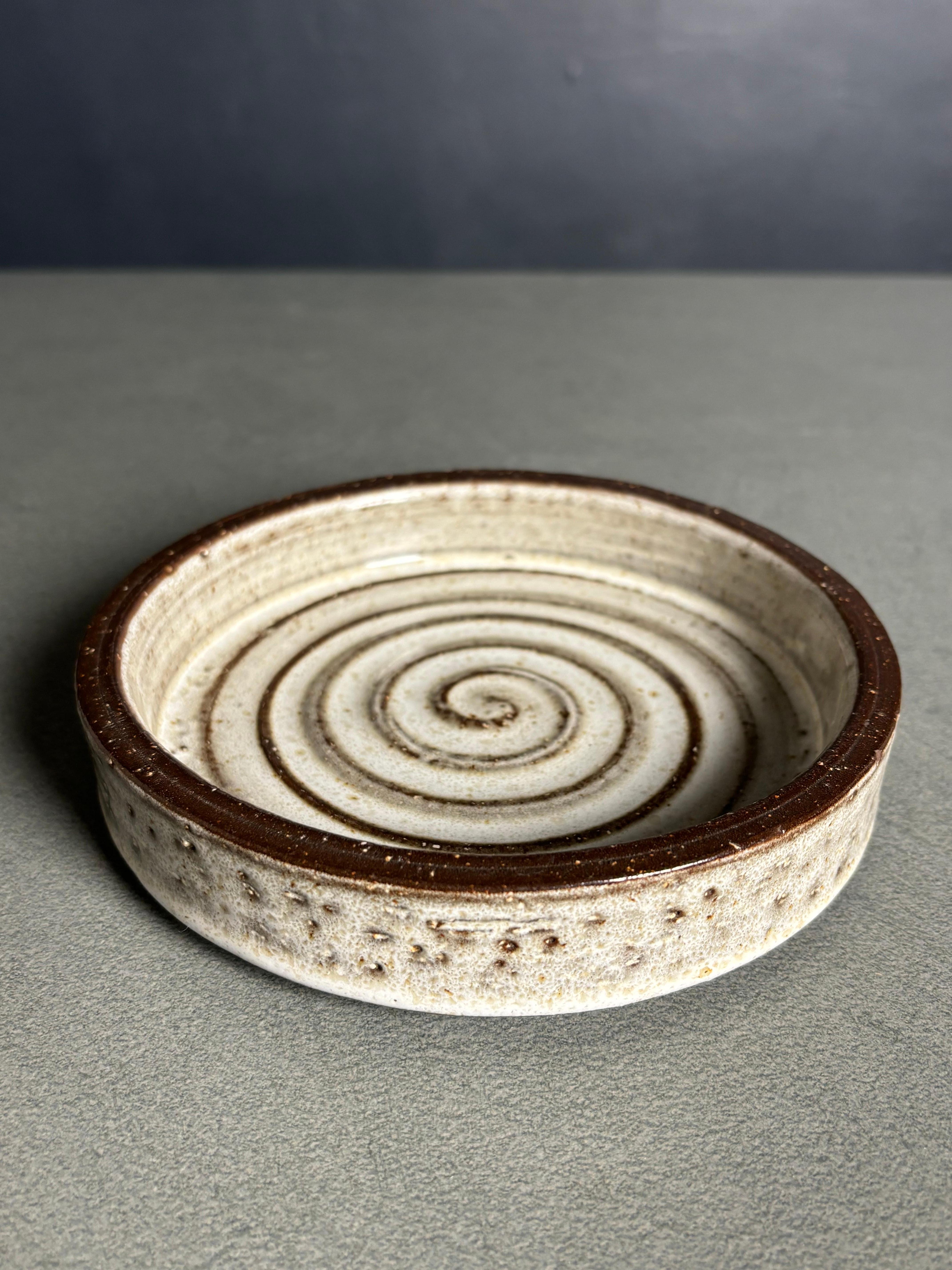 Hand-thrown Danish midcentury modern stoneware vide-poche bowl. Sandy light gray glaze over spiral relief decor in the center and clear glaze on the sides over the dark brown material. Manufactured by Michael Andersen & Son on the island of Bornholm