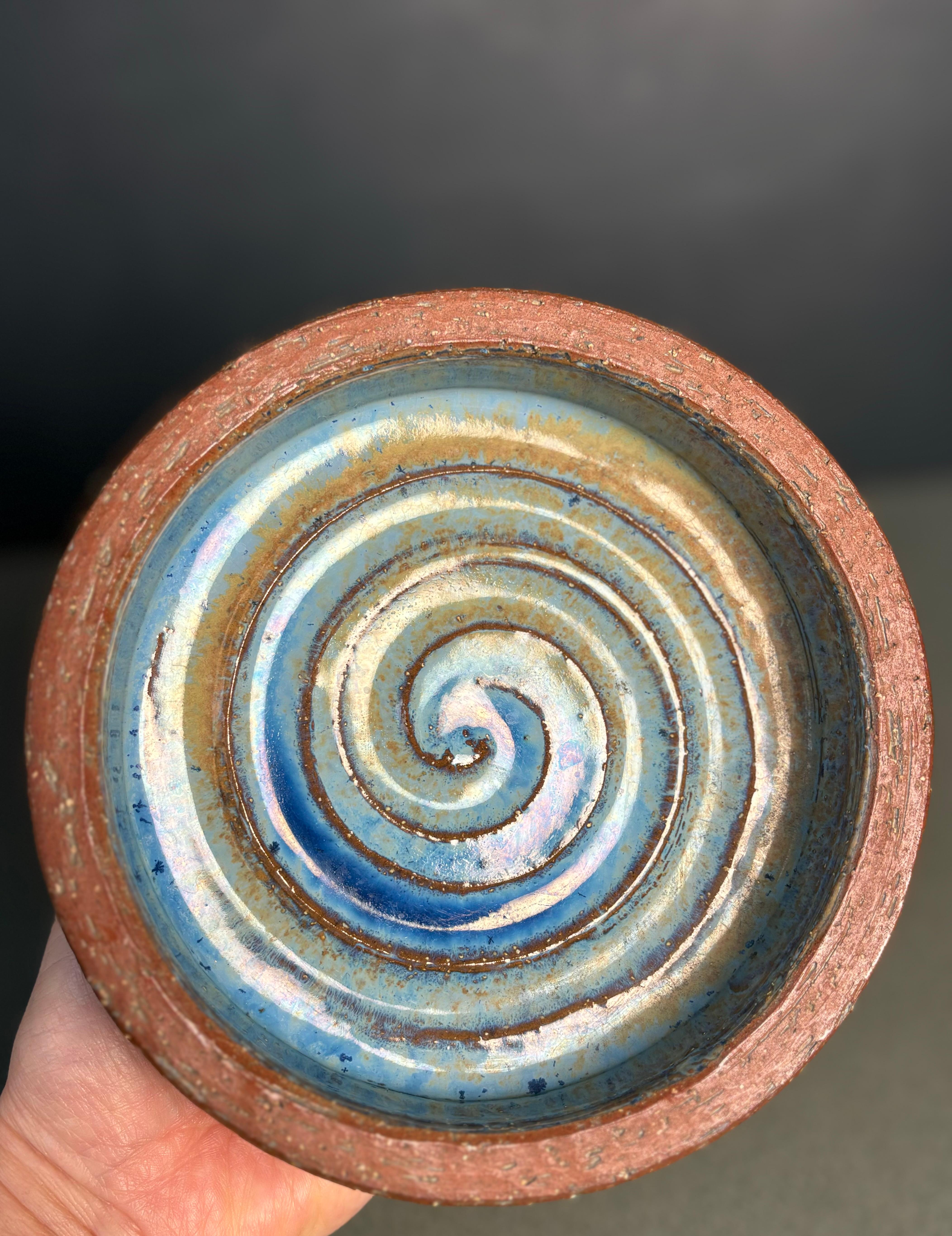 Hand-thrown Danish midcentury modern stoneware vide-poche bowl. Shiny light blue and sandy yellow glaze over spiral relief decor in the center and clear glaze on the sides over the dark brown material. Manufactured by Michael Andersen & Son on the