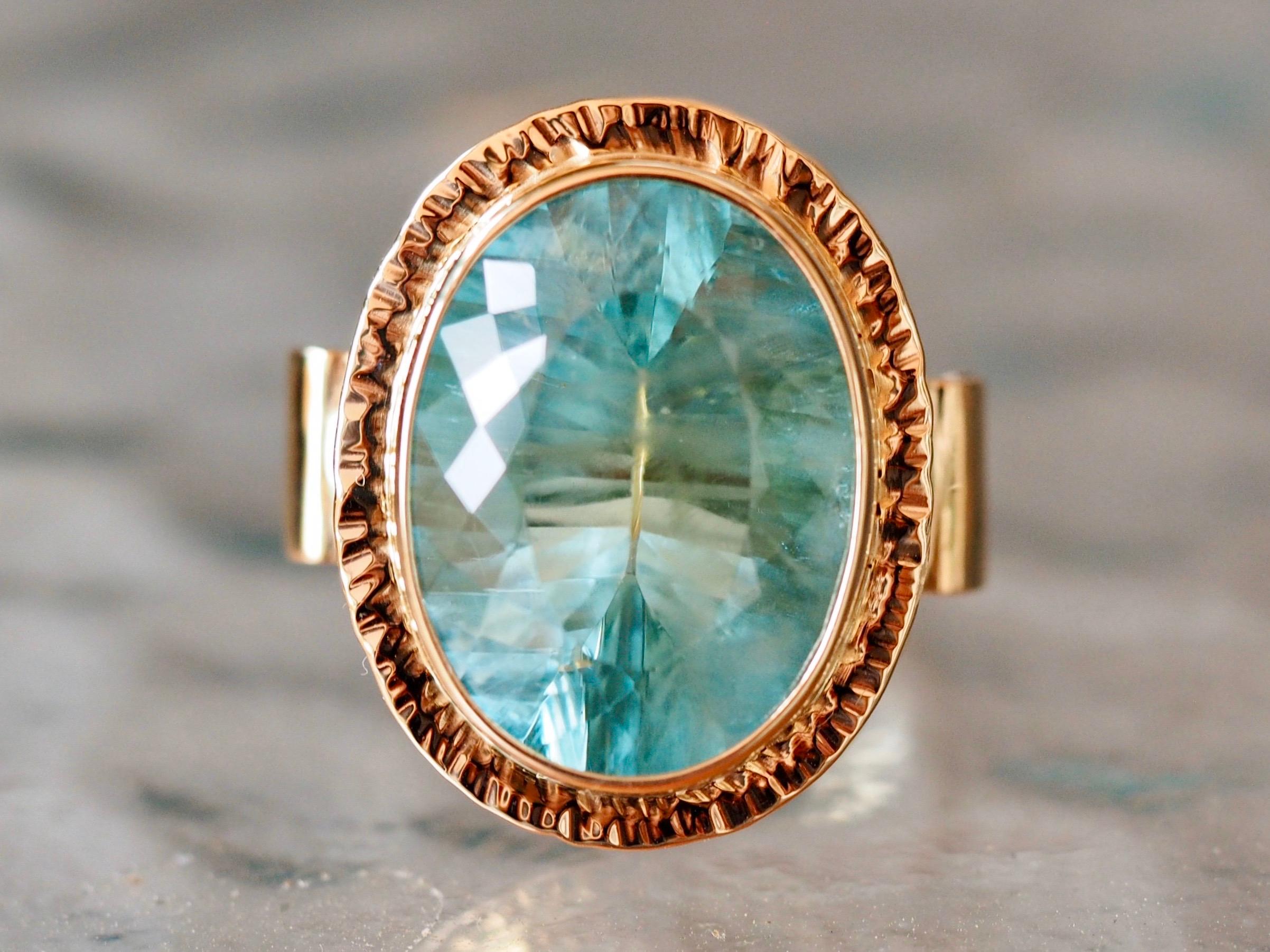 Designer Bakso statement ring holds a large faceted oval faceted blue tourmaline that measures 19 x 15 MM , weighing 20 carats. The light Caribbean blue center is bezel set in a 14-Karat yellow gold frame, it is detailed with a hammered golden