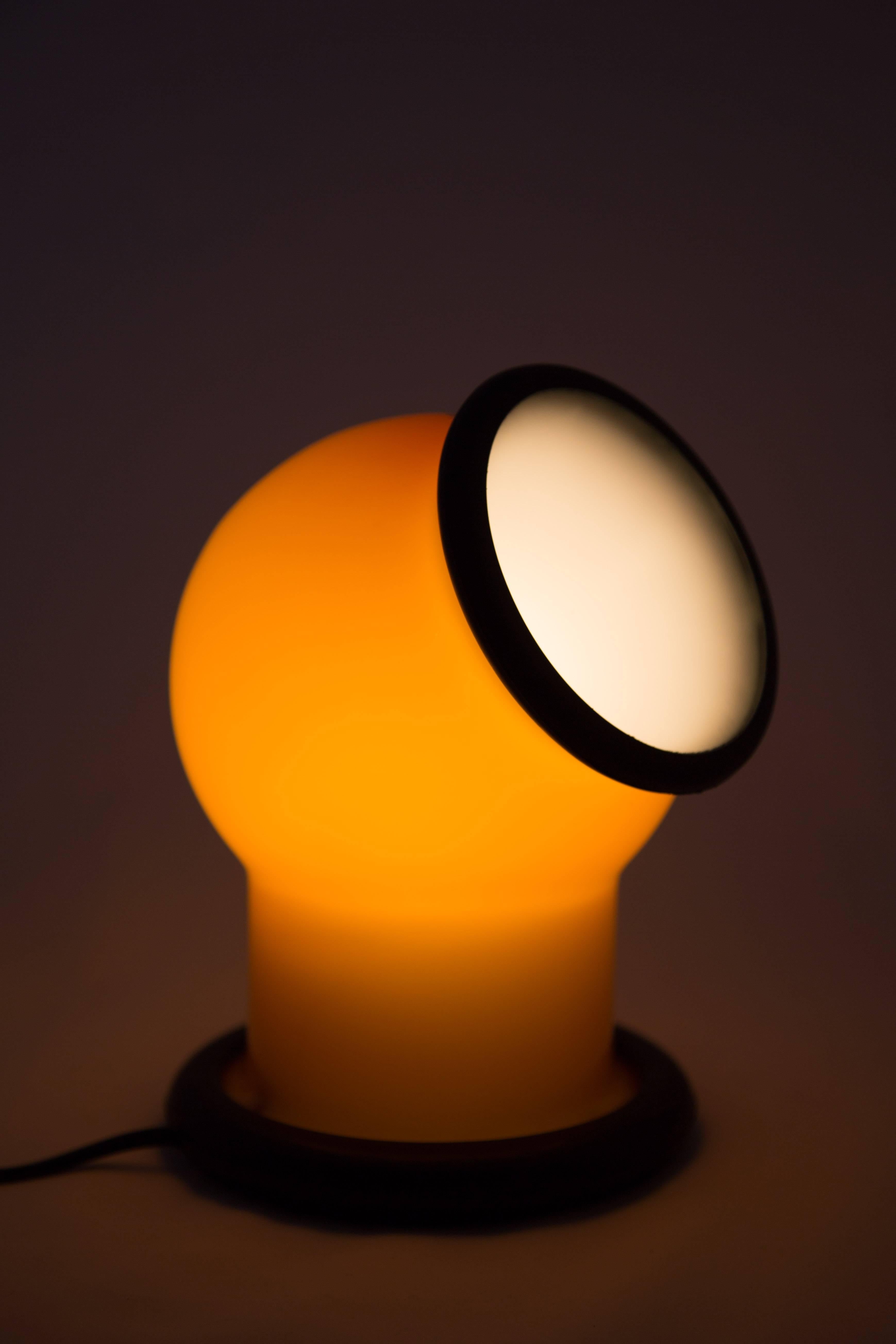 Michael Bang Epoke table lamp for Holmegaard with orange glass and rubber. The lamp looks like the pipe of a submarine. The form is very cheerful. The lamp is of glass with rubber rings.
