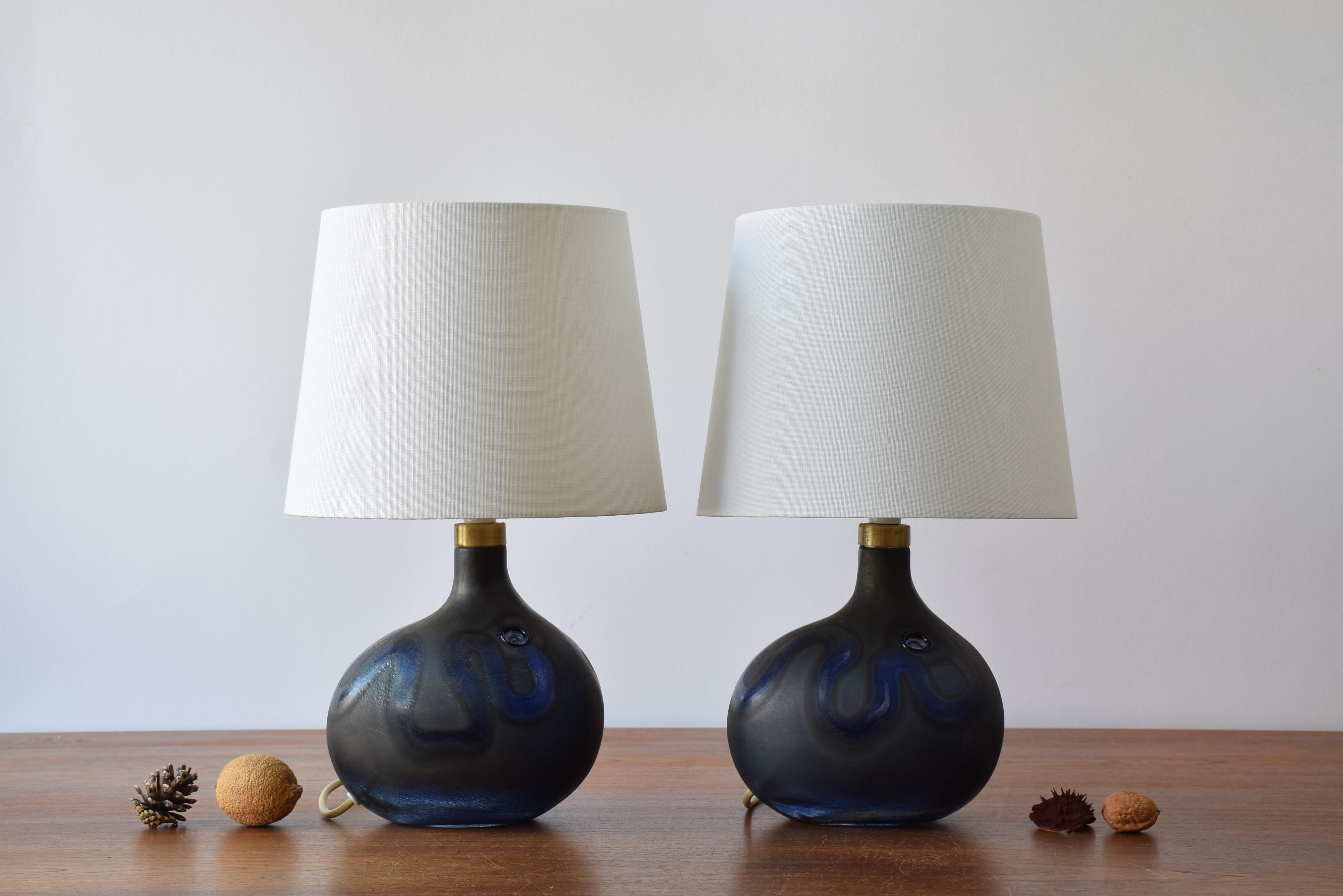 Pair of midcentury Danish sculptural hand blown glass lamps designed by Michael Bang and made by Holmegaard. They were only in production shortly from 1973-1976.

The lamps have a matte blue grey surface with a polished glass ribbon and a hole