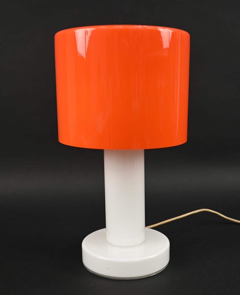 Add a fun pop of color to your interior with this playful table lamp designed by Michael Bang for Holmegaard. This model Rolino-Maxi lamp features a striking orange glass shade with a white cased glass base. 
With Holmegaard label underneath.